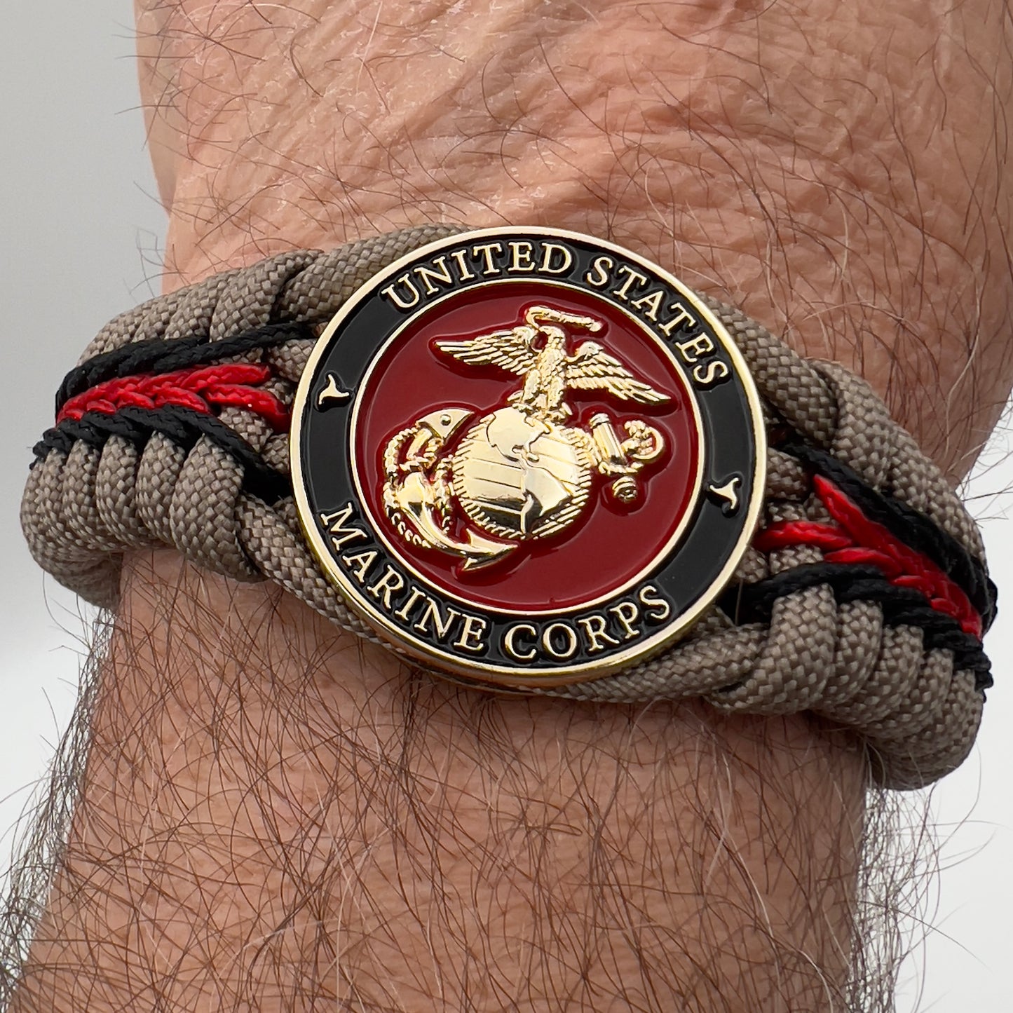 Thick, rigid and comfortable braided United States Marine Corps bracelet featuring a 24K gold plated USMC Eagle Globe and Anchor medallion, a gold Cobra style tactical buckle and woven with tan 550 paracord and Imperial Red and black micro cord.