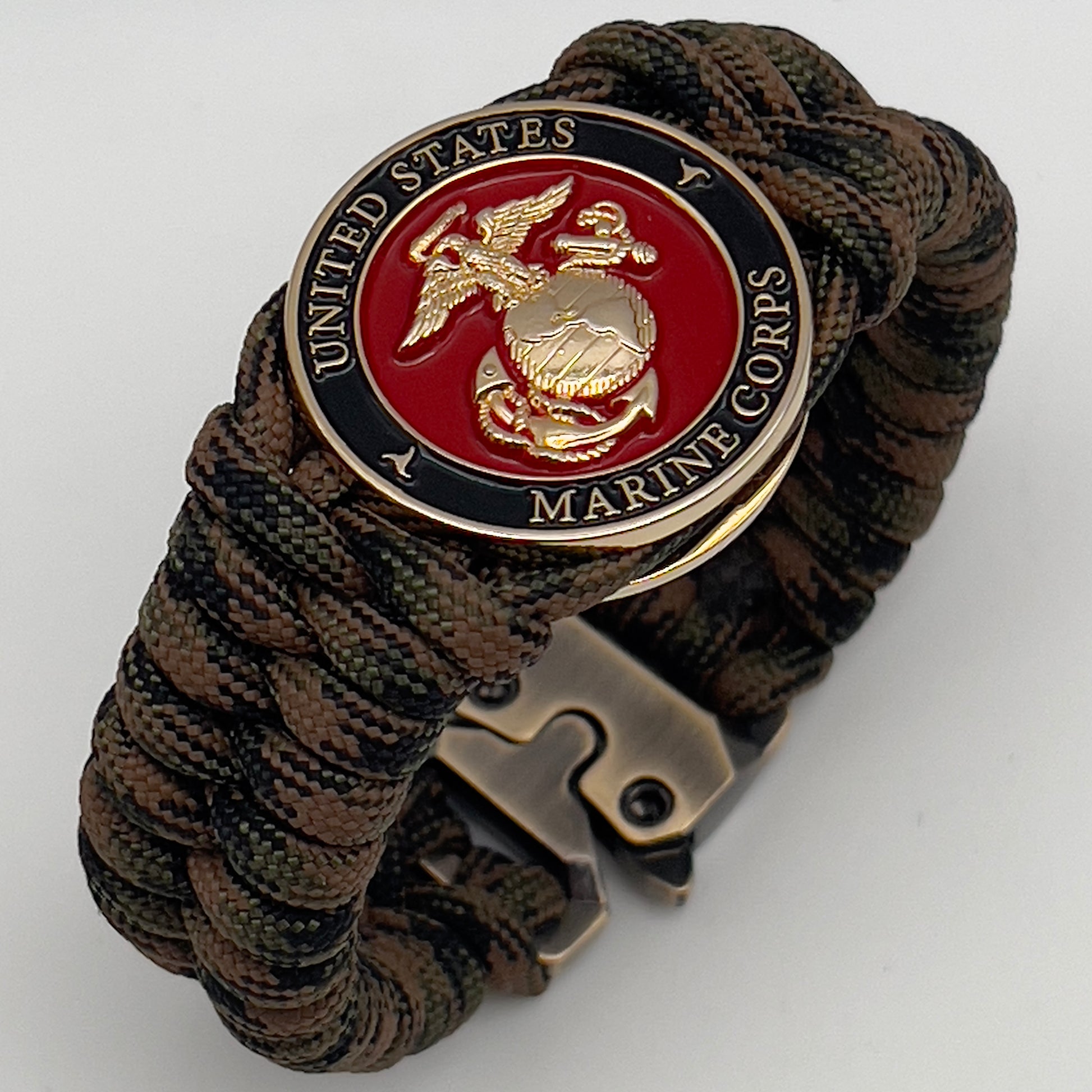 Thick, semi-rigid and comfortable braided United States Marine Corps bracelet featuring a 24K gold plated USMC Eagle Globe and Anchor medallion, a gold Cobra style tactical buckle and woven with Woodland camo 550 paracord.