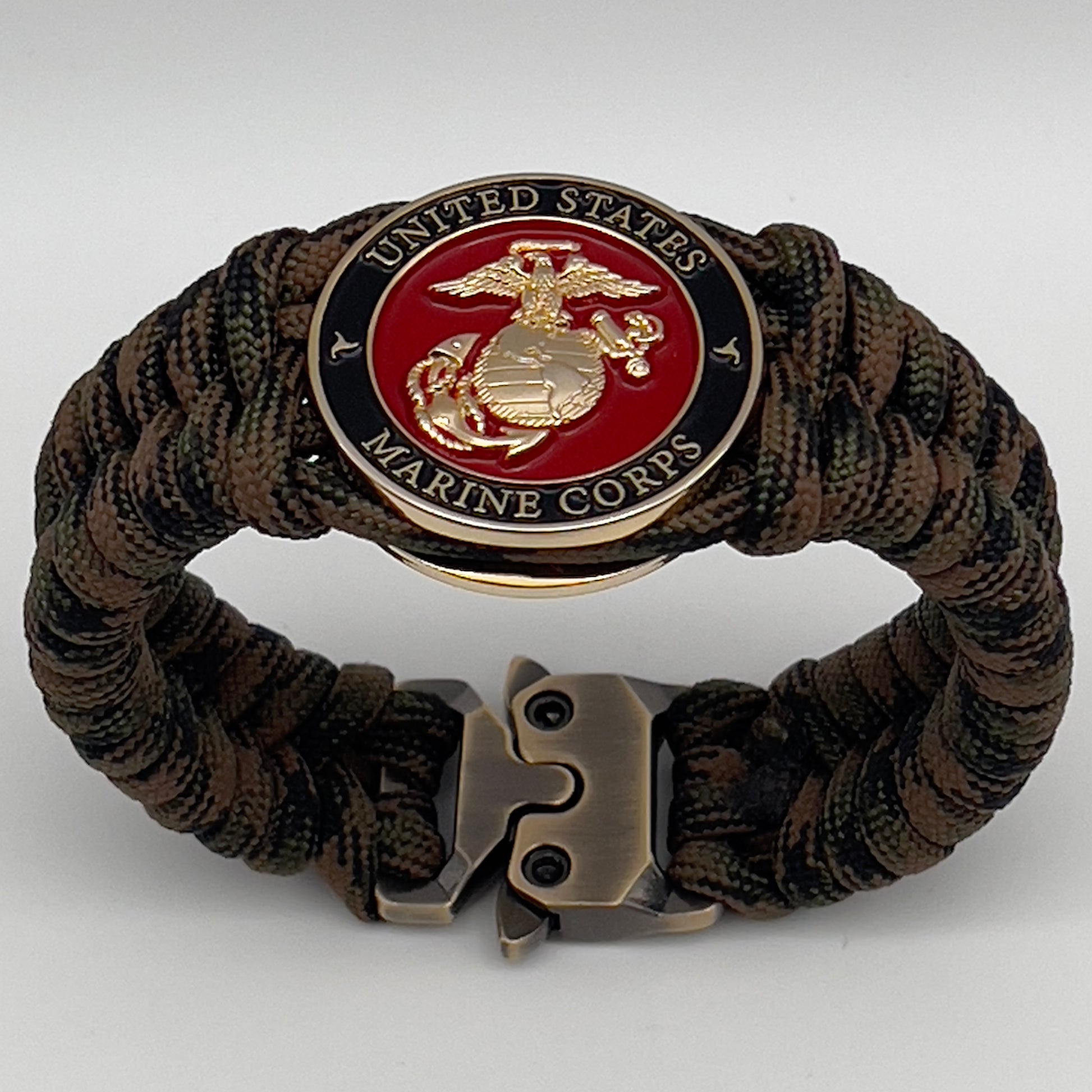 Thick, semi-rigid and comfortable braided United States Marine Corps bracelet featuring a 24K gold plated USMC Eagle Globe and Anchor medallion, a gold Cobra style tactical buckle and woven with Woodland camo 550 paracord.
