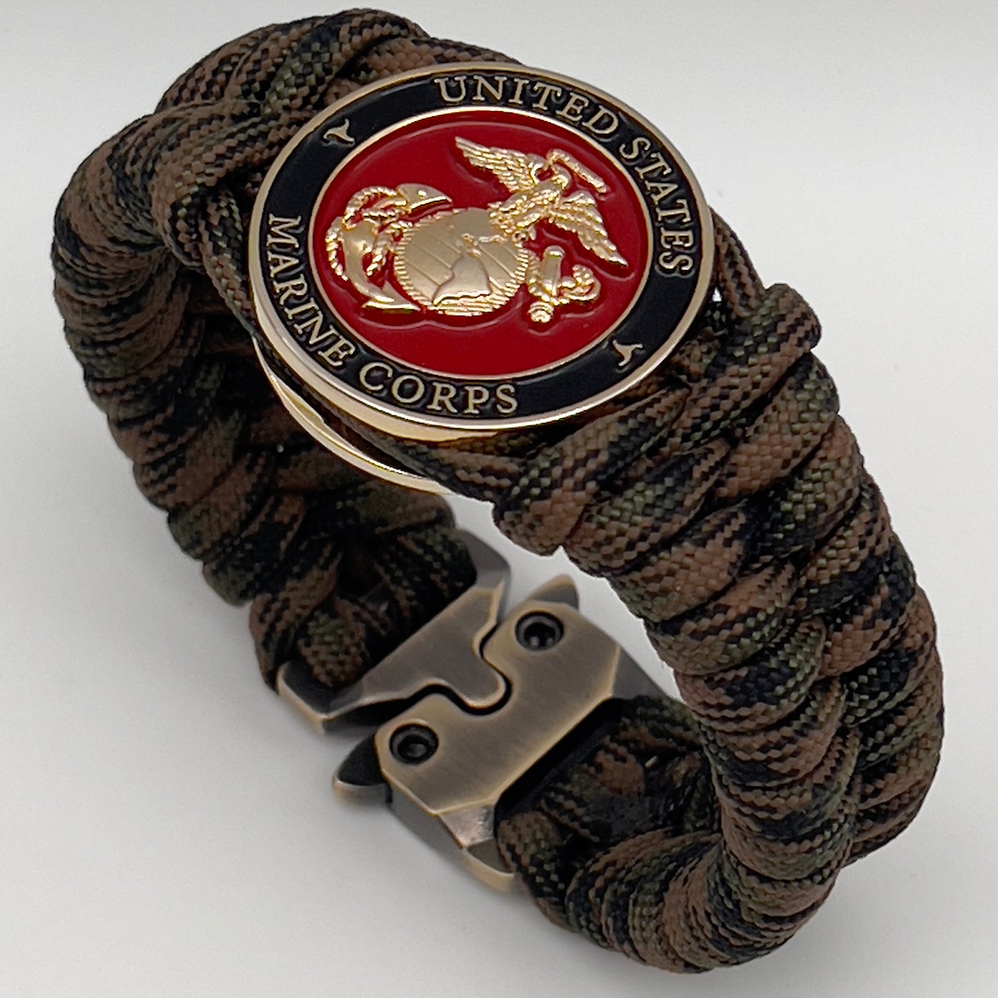 Thick, semi-rigid and comfortable braided United States Marine Corps bracelet featuring a 24K gold plated USMC Eagle Globe and Anchor medallion, a gold Cobra style tactical buckle and woven with Woodland camo 550 paracord.