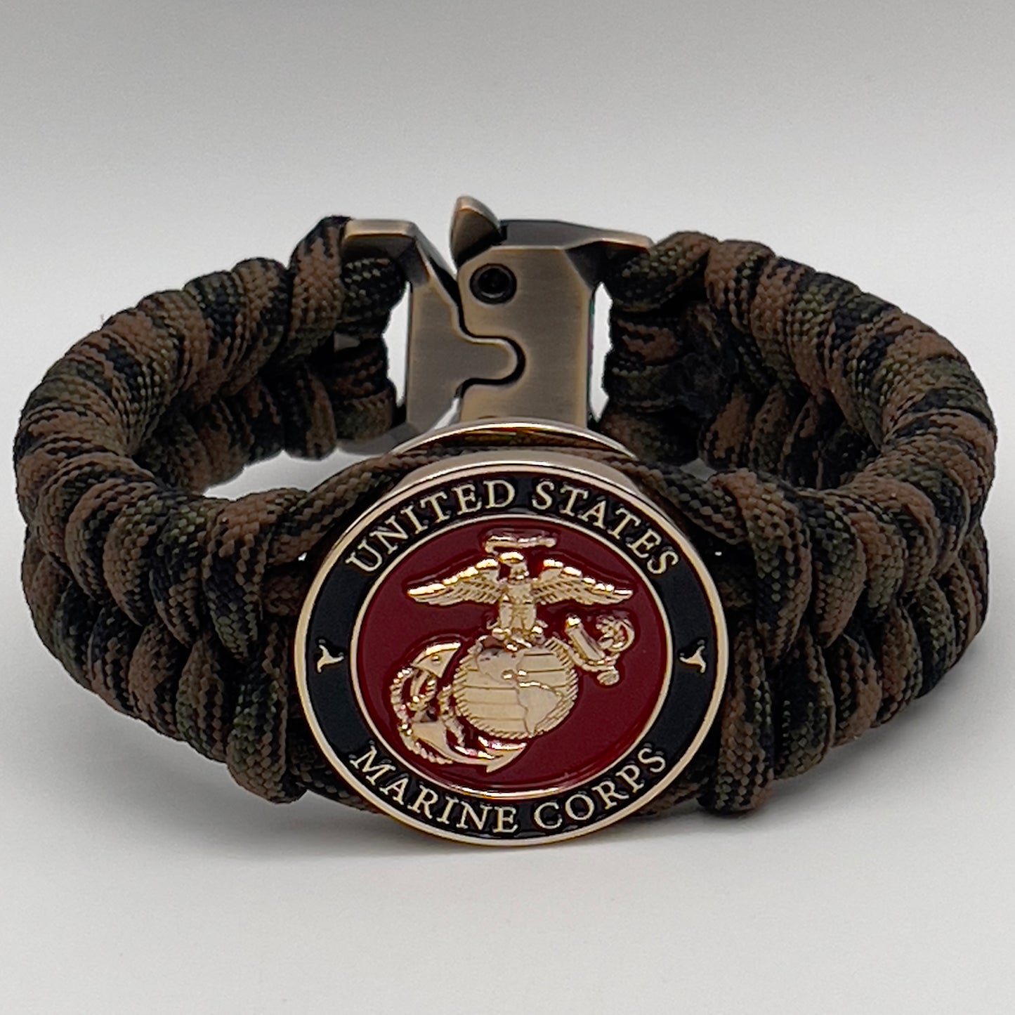 Thick, semi-rigid and comfortable braided United States Marine Corps bracelet featuring a 24K gold plated USMC Eagle Globe and Anchor medallion, a gold Cobra style tactical buckle and woven with Woodland camo 550 paracord.