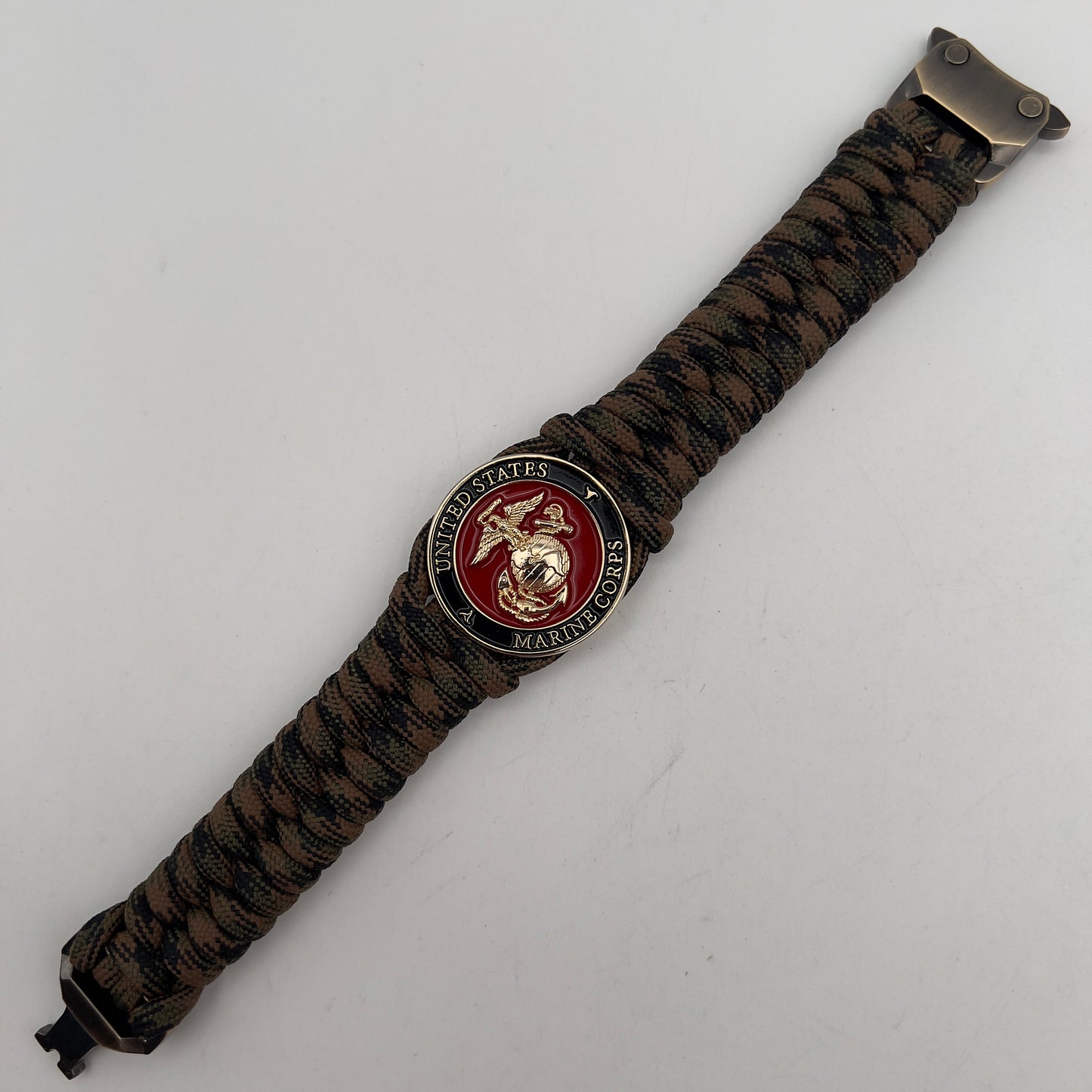 Thick, semi-rigid and comfortable braided United States Marine Corps bracelet featuring a 24K gold plated USMC Eagle Globe and Anchor medallion, a gold Cobra style tactical buckle and woven with Woodland camo 550 paracord.