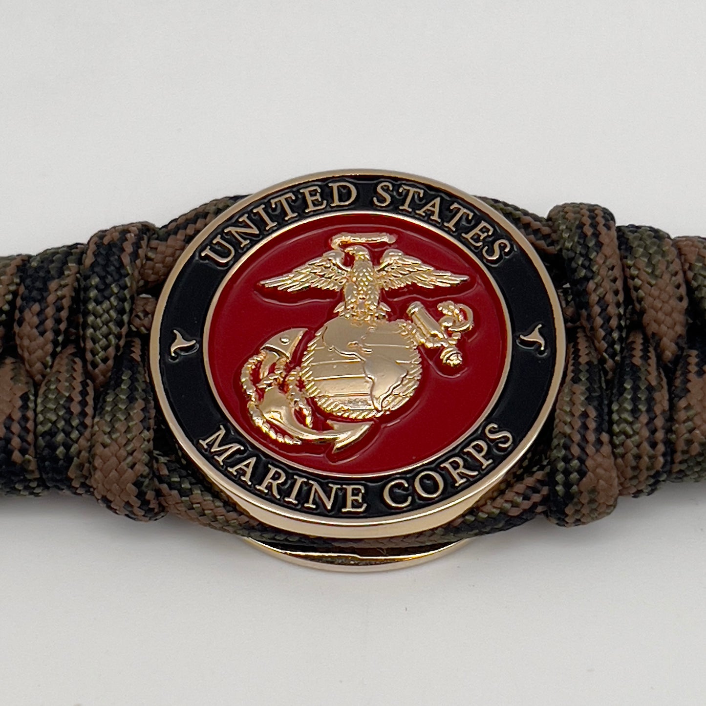 Thick, semi-rigid and comfortable braided United States Marine Corps bracelet featuring a 24K gold plated USMC Eagle Globe and Anchor medallion, a gold Cobra style tactical buckle and woven with Woodland camo 550 paracord.