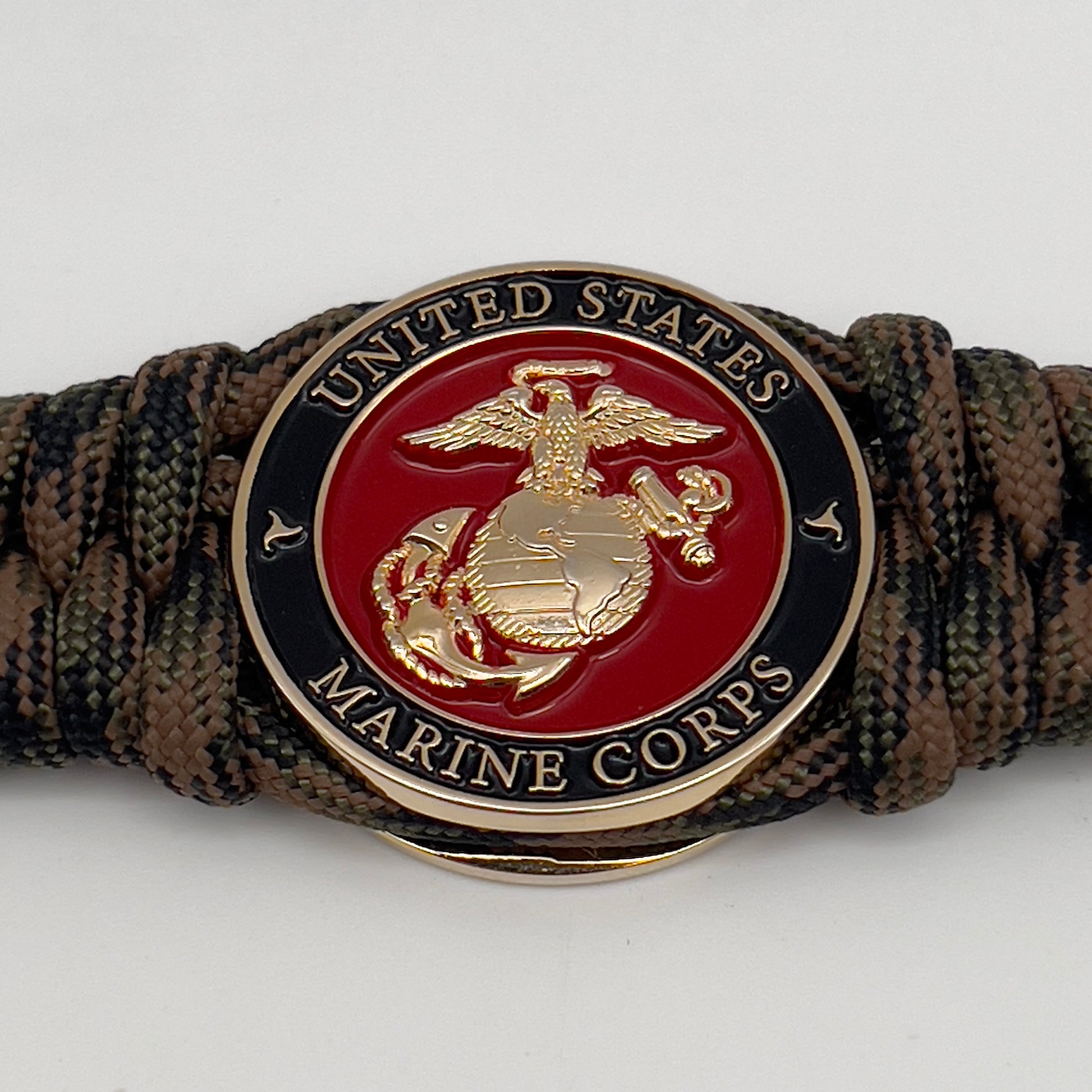 Thick, semi-rigid and comfortable braided United States Marine Corps bracelet featuring a 24K gold plated USMC Eagle Globe and Anchor medallion, a gold Cobra style tactical buckle and woven with Woodland camo 550 paracord.