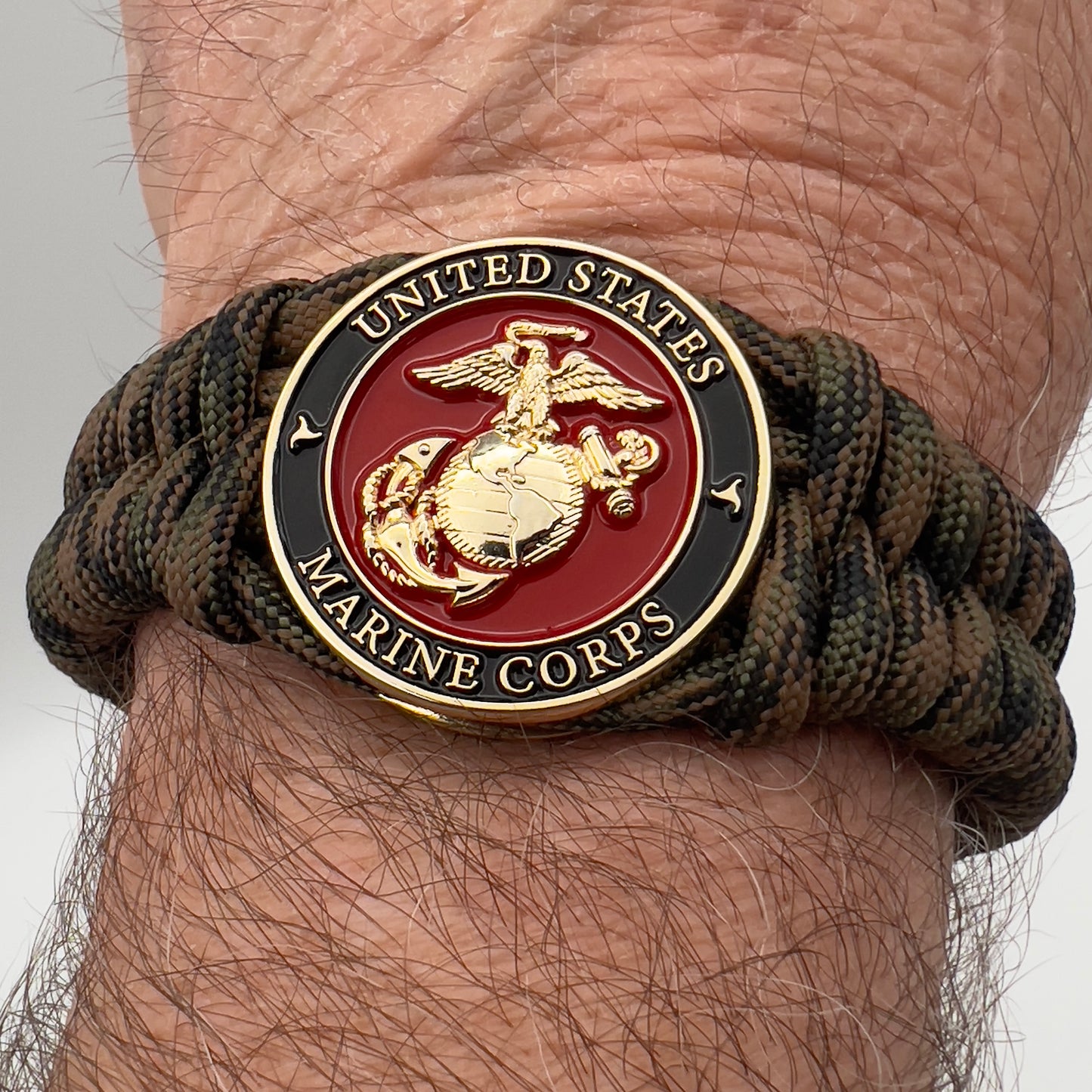 Thick, semi-rigid and comfortable braided United States Marine Corps bracelet featuring a 24K gold plated USMC Eagle Globe and Anchor medallion, a gold Cobra style tactical buckle and woven with Woodland camo 550 paracord.
