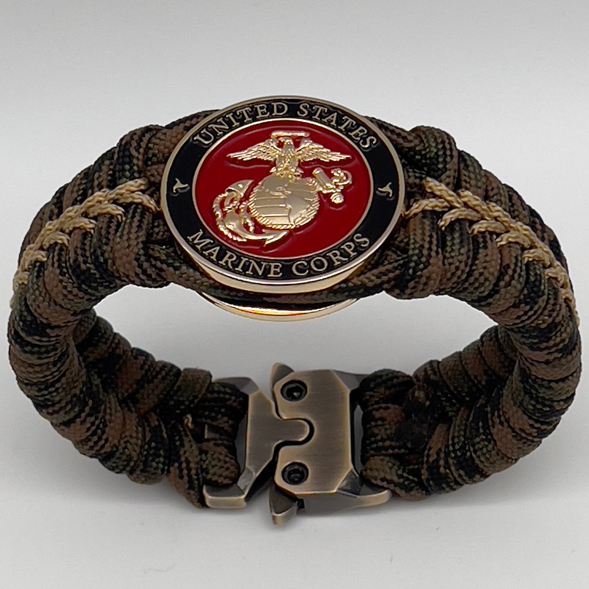 Thick, rigid and comfortable braided United States Marine Corps bracelet featuring a 24K gold plated USMC Eagle Globe and Anchor medallion, a gold Cobra style tactical buckle and woven with Woodland 550 paracord.