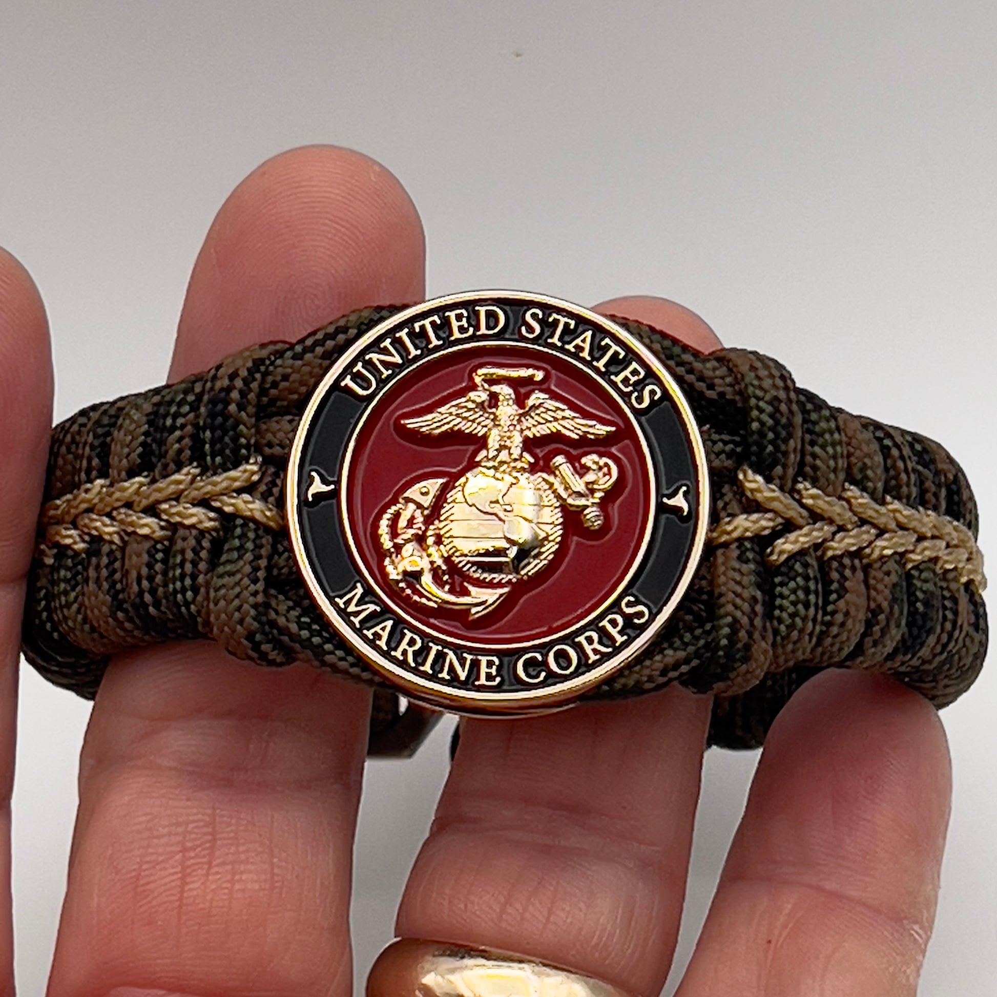 Thick, rigid and comfortable braided United States Marine Corps bracelet featuring a 24K gold plated USMC Eagle Globe and Anchor medallion, a gold Cobra style tactical buckle and woven with Woodland 550 paracord.
