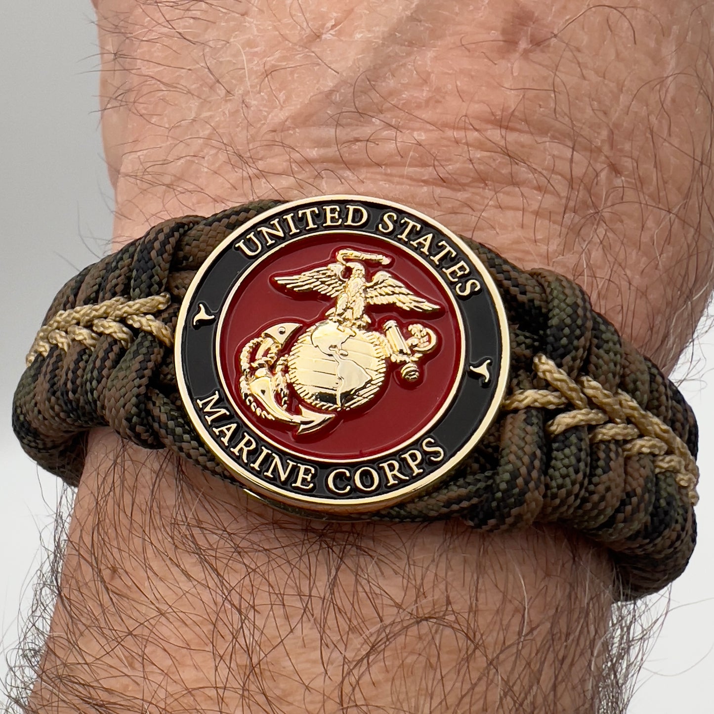 Thick, rigid and comfortable braided United States Marine Corps bracelet featuring a 24K gold plated USMC Eagle Globe and Anchor medallion, a gold Cobra style tactical buckle and woven with Woodland 550 paracord.