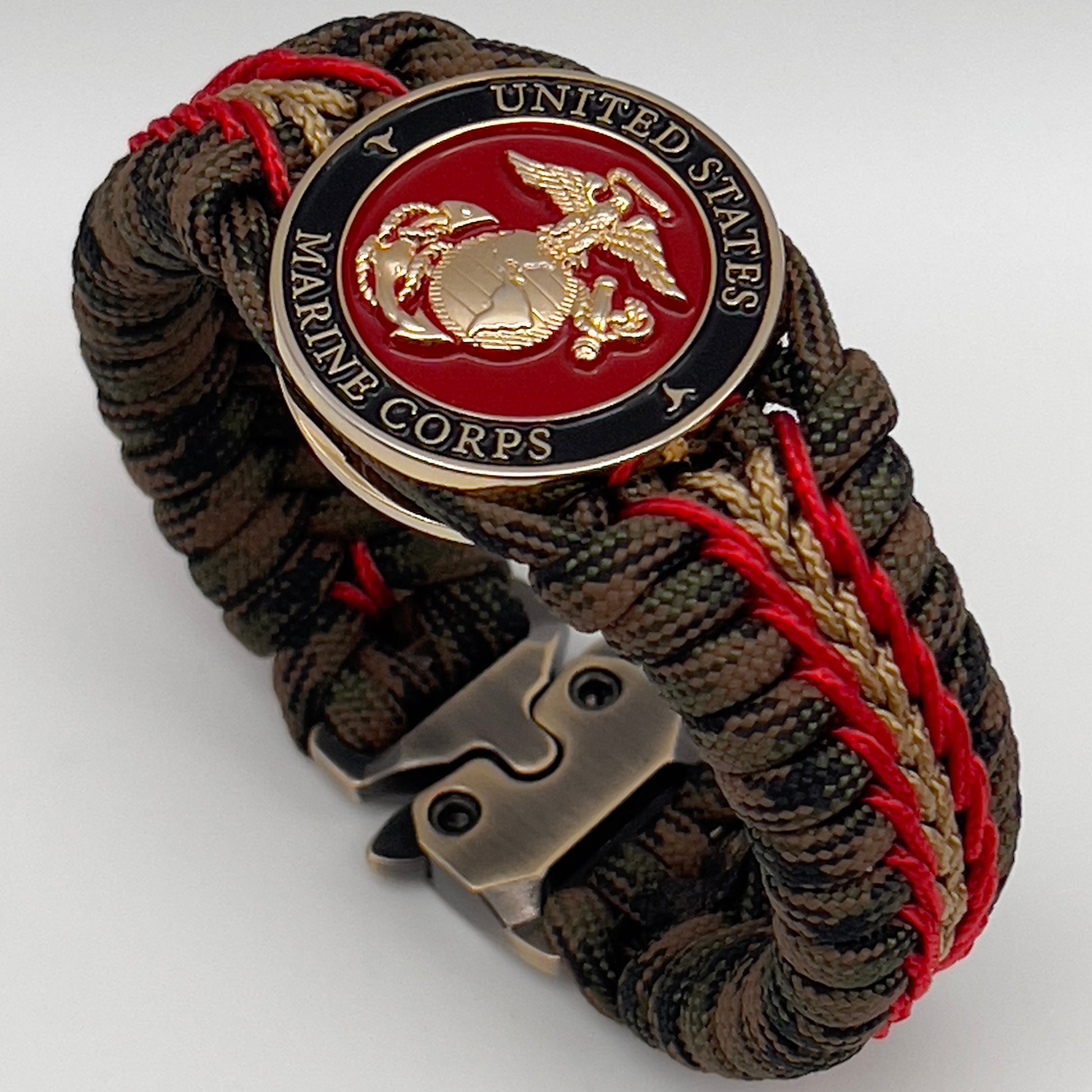 Thick, rigid and comfortable braided United States Marine Corps bracelet featuring a 24K gold plated USMC Eagle Globe and Anchor medallion, a gold Cobra style tactical buckle and woven with Woodland camo 550 paracord and Imperial Red and Gold micro cord.