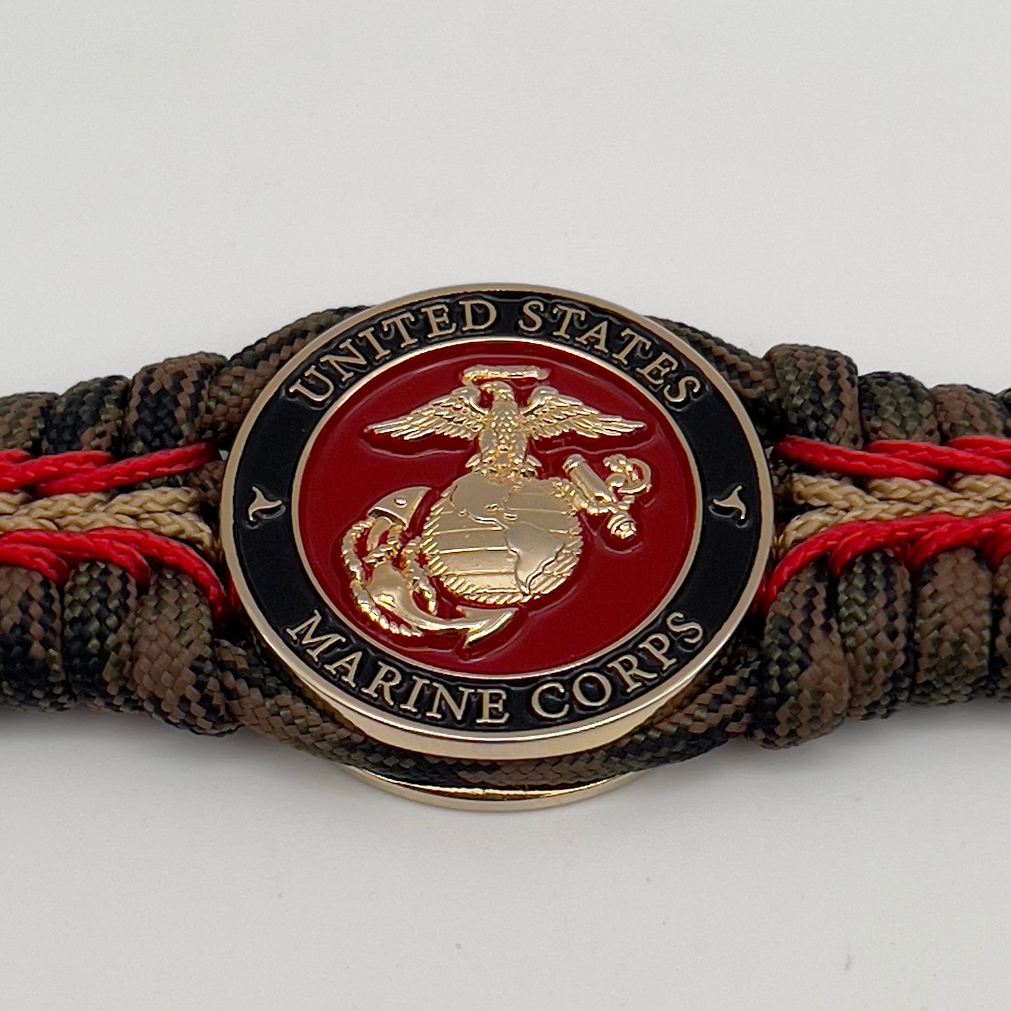 Thick, rigid and comfortable braided United States Marine Corps bracelet featuring a 24K gold plated USMC Eagle Globe and Anchor medallion, a gold Cobra style tactical buckle and woven with Woodland camo 550 paracord and Imperial Red and Gold micro cord.