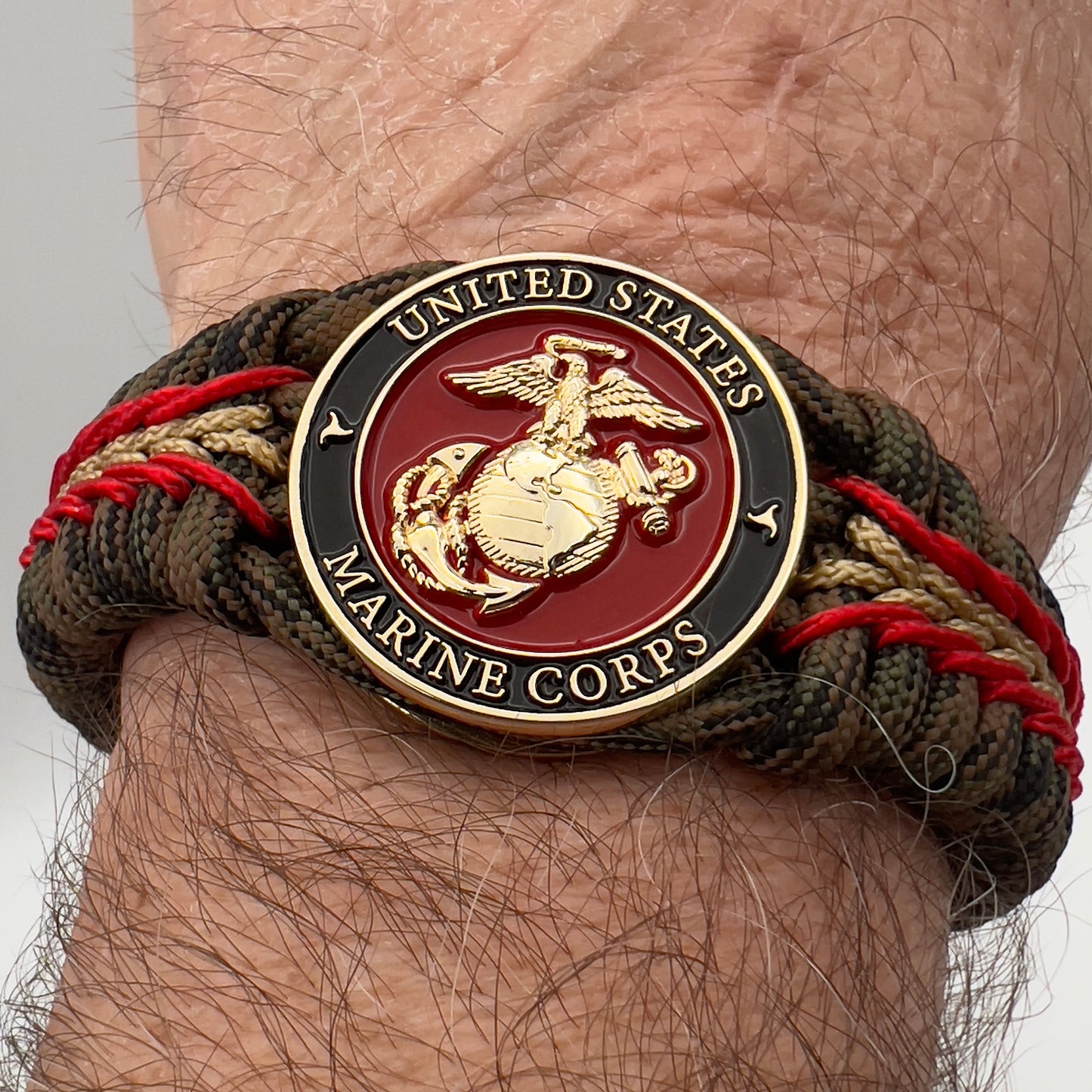 Thick, rigid and comfortable braided United States Marine Corps bracelet featuring a 24K gold plated USMC Eagle Globe and Anchor medallion, a gold Cobra style tactical buckle and woven with Woodland camo 550 paracord and Imperial Red and Gold micro cord.