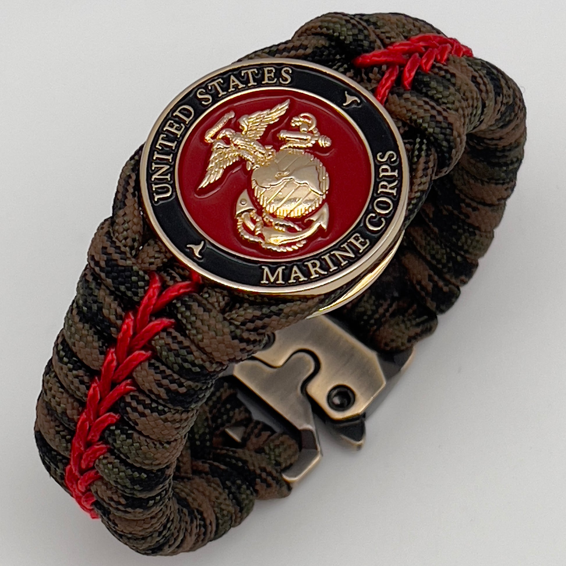 Thick, rigid and comfortable braided United States Marine Corps bracelet featuring a 24K gold plated USMC Eagle Globe and Anchor medallion, a gold Cobra style tactical buckle and woven with Woodland Camo 550 paracord and Imperial Red micro cord.