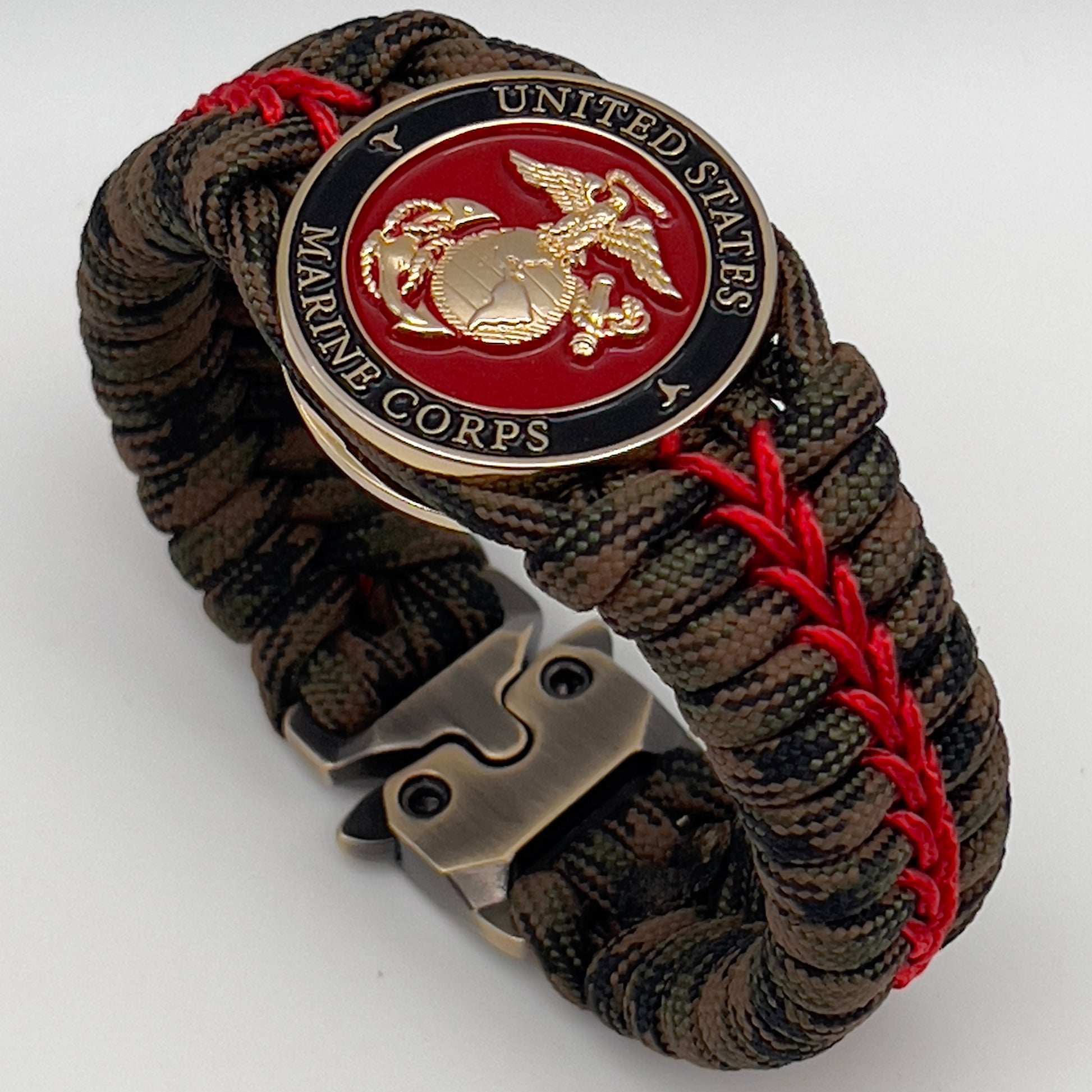 Thick, rigid and comfortable braided United States Marine Corps bracelet featuring a 24K gold plated USMC Eagle Globe and Anchor medallion, a gold Cobra style tactical buckle and woven with Woodland Camo 550 paracord and Imperial Red micro cord.