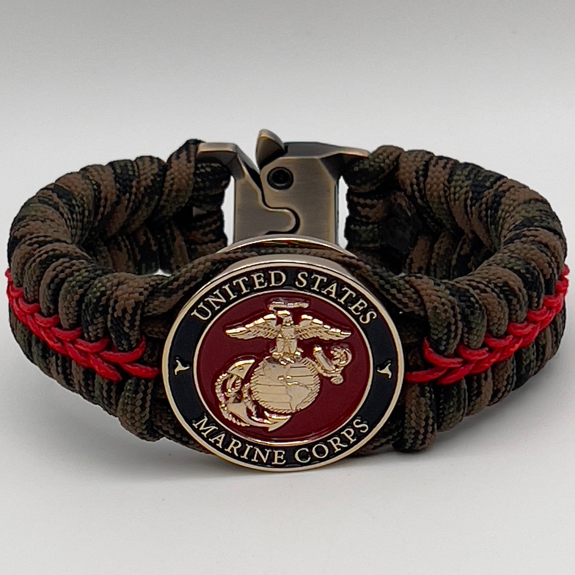 Thick, rigid and comfortable braided United States Marine Corps bracelet featuring a 24K gold plated USMC Eagle Globe and Anchor medallion, a gold Cobra style tactical buckle and woven with Woodland Camo 550 paracord and Imperial Red micro cord.