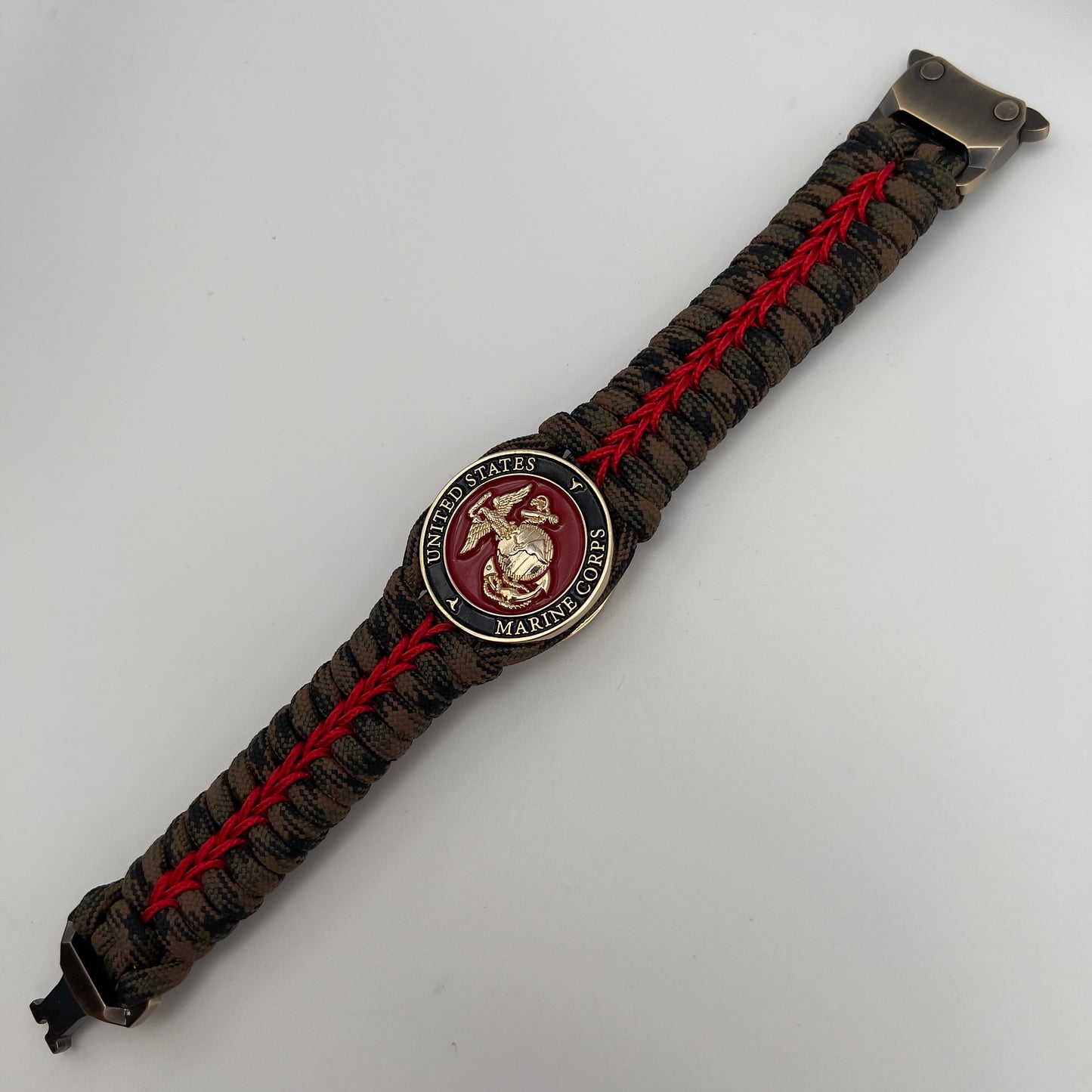 Thick, rigid and comfortable braided United States Marine Corps bracelet featuring a 24K gold plated USMC Eagle Globe and Anchor medallion, a gold Cobra style tactical buckle and woven with Woodland Camo 550 paracord and Imperial Red micro cord.