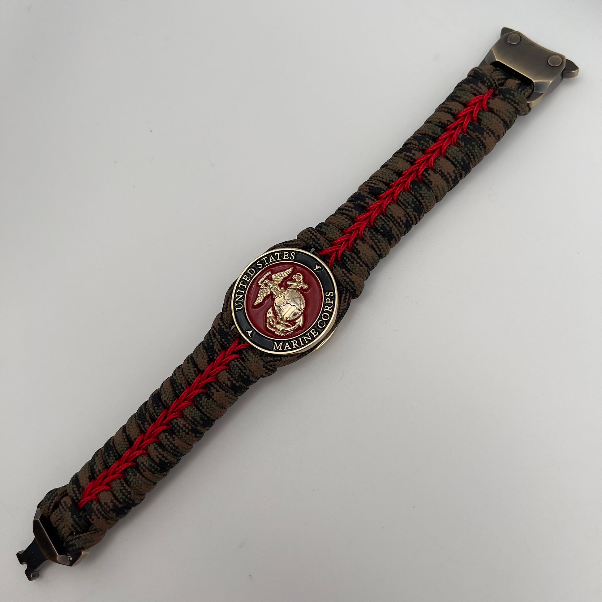 Thick, rigid and comfortable braided United States Marine Corps bracelet featuring a 24K gold plated USMC Eagle Globe and Anchor medallion, a gold Cobra style tactical buckle and woven with Woodland Camo 550 paracord and Imperial Red micro cord.