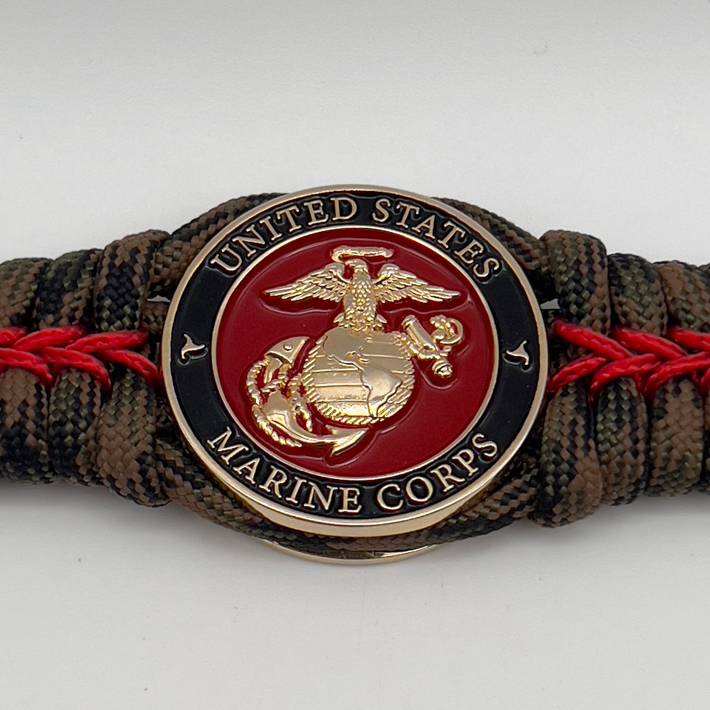 Thick, rigid and comfortable braided United States Marine Corps bracelet featuring a 24K gold plated USMC Eagle Globe and Anchor medallion, a gold Cobra style tactical buckle and woven with Woodland Camo 550 paracord and Imperial Red micro cord.