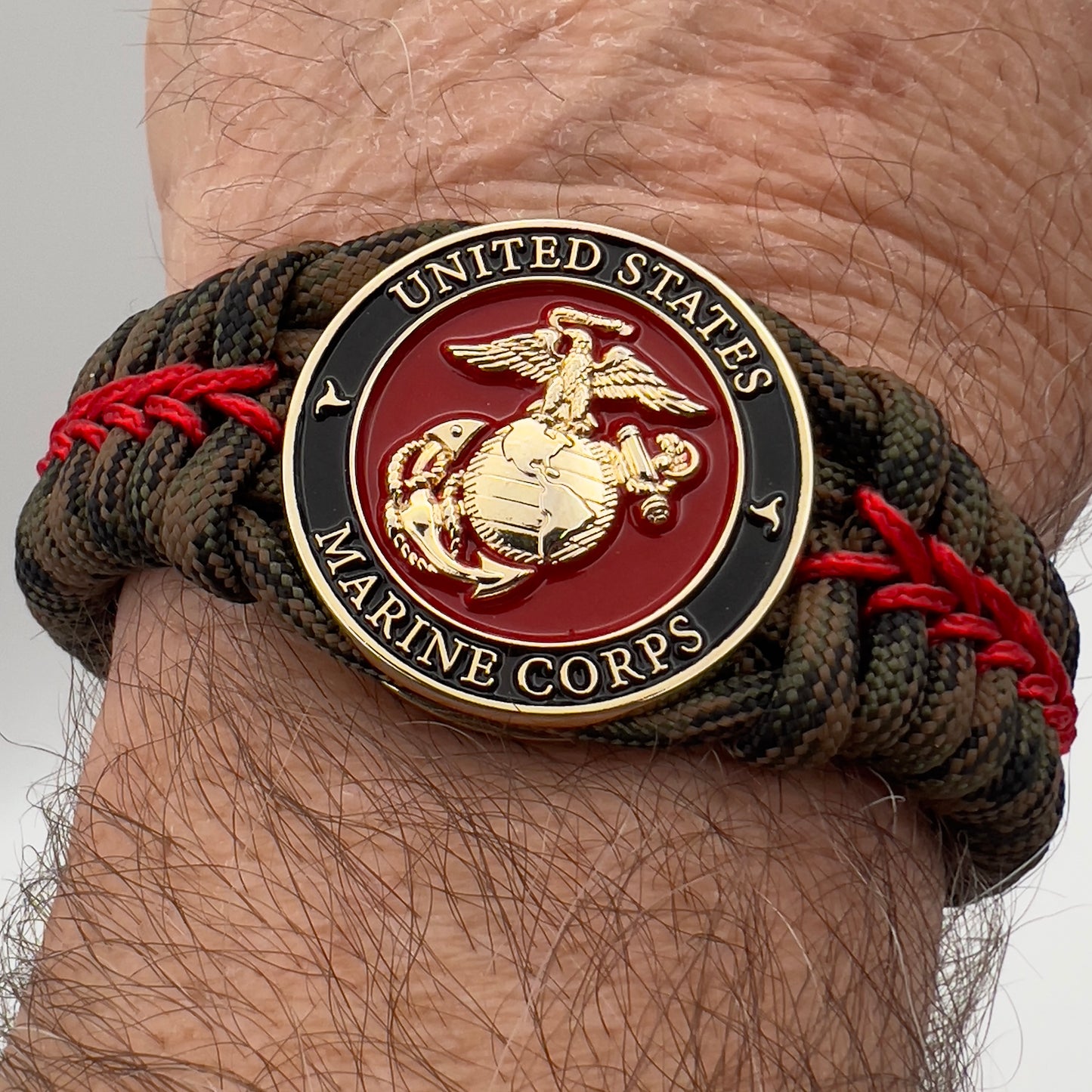 Thick, rigid and comfortable braided United States Marine Corps bracelet featuring a 24K gold plated USMC Eagle Globe and Anchor medallion, a gold Cobra style tactical buckle and woven with Woodland Camo 550 paracord and Imperial Red micro cord.