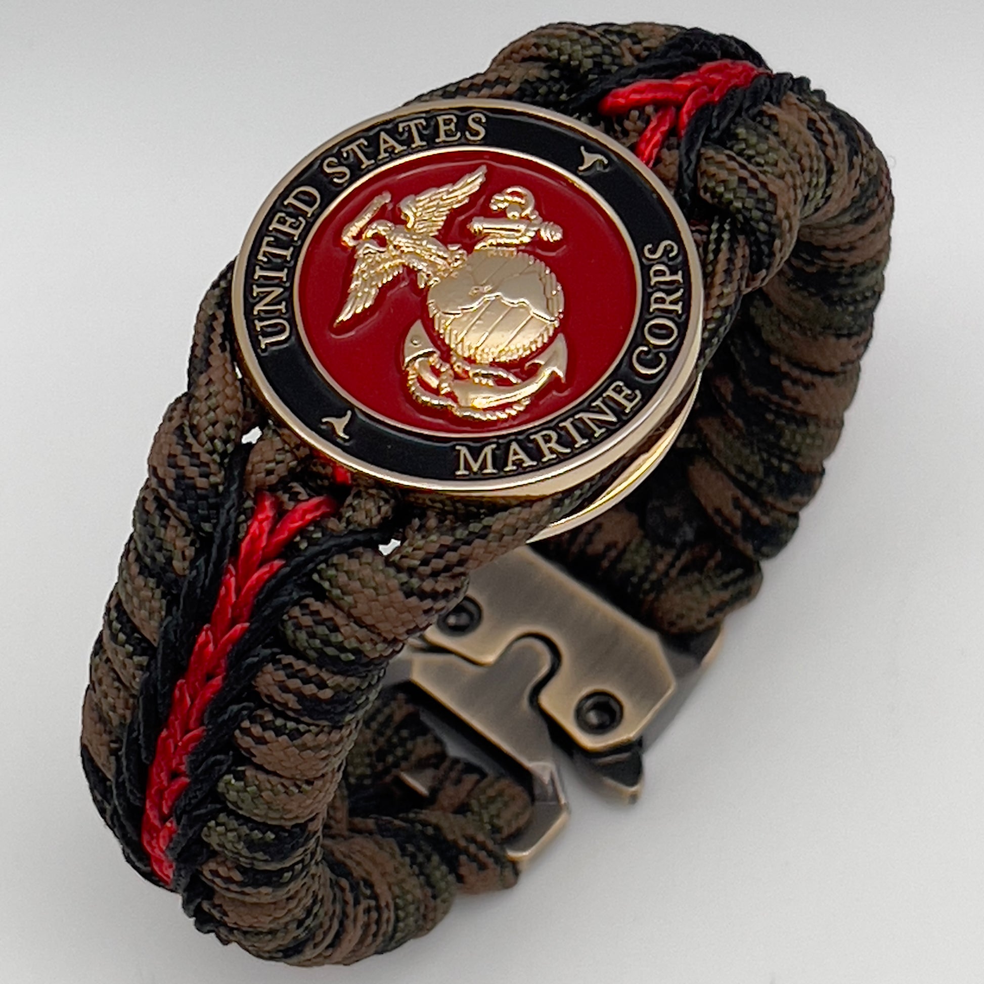 Thick, semi-rigid and comfortable braided United States Marine Corps bracelet featuring a 24K gold plated USMC Eagle Globe and Anchor medallion, a gold Cobra style tactical buckle and woven with Woodland camo 550 paracord and black and Imperial red micro cord.