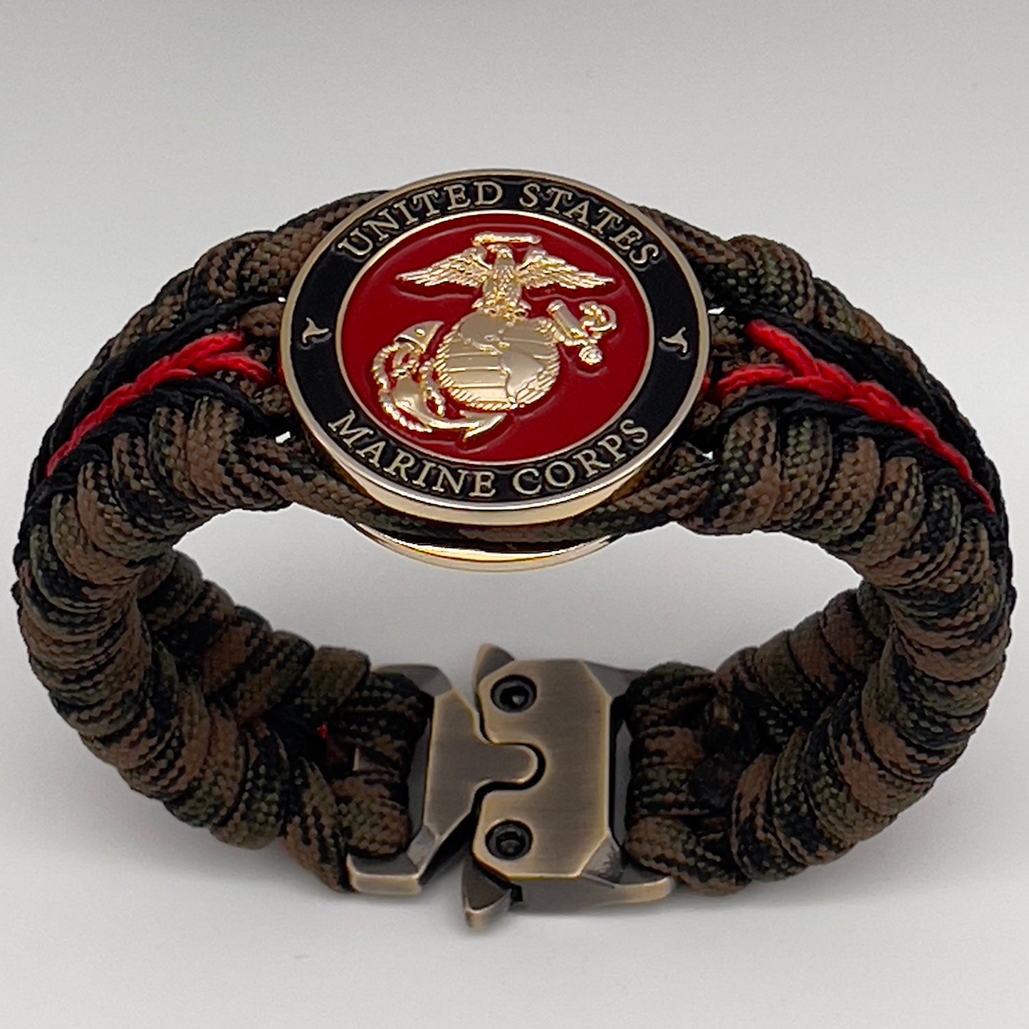 Thick, semi-rigid and comfortable braided United States Marine Corps bracelet featuring a 24K gold plated USMC Eagle Globe and Anchor medallion, a gold Cobra style tactical buckle and woven with Woodland camo 550 paracord and black and Imperial red micro cord.