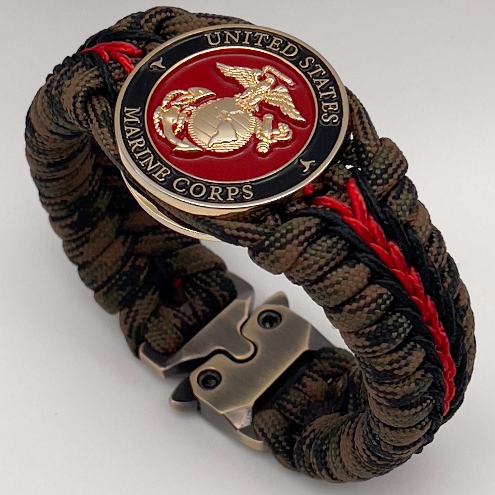 Thick, semi-rigid and comfortable braided United States Marine Corps bracelet featuring a 24K gold plated USMC Eagle Globe and Anchor medallion, a gold Cobra style tactical buckle and woven with Woodland camo 550 paracord and black and Imperial red micro cord.