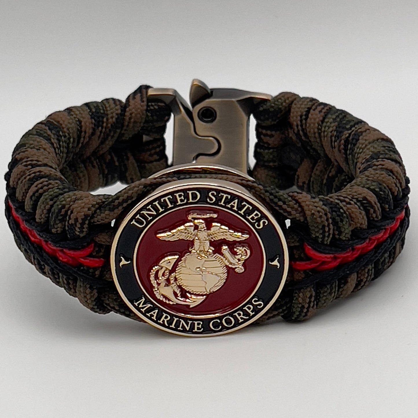 Thick, semi-rigid and comfortable braided United States Marine Corps bracelet featuring a 24K gold plated USMC Eagle Globe and Anchor medallion, a gold Cobra style tactical buckle and woven with Woodland camo 550 paracord and black and Imperial red micro cord.