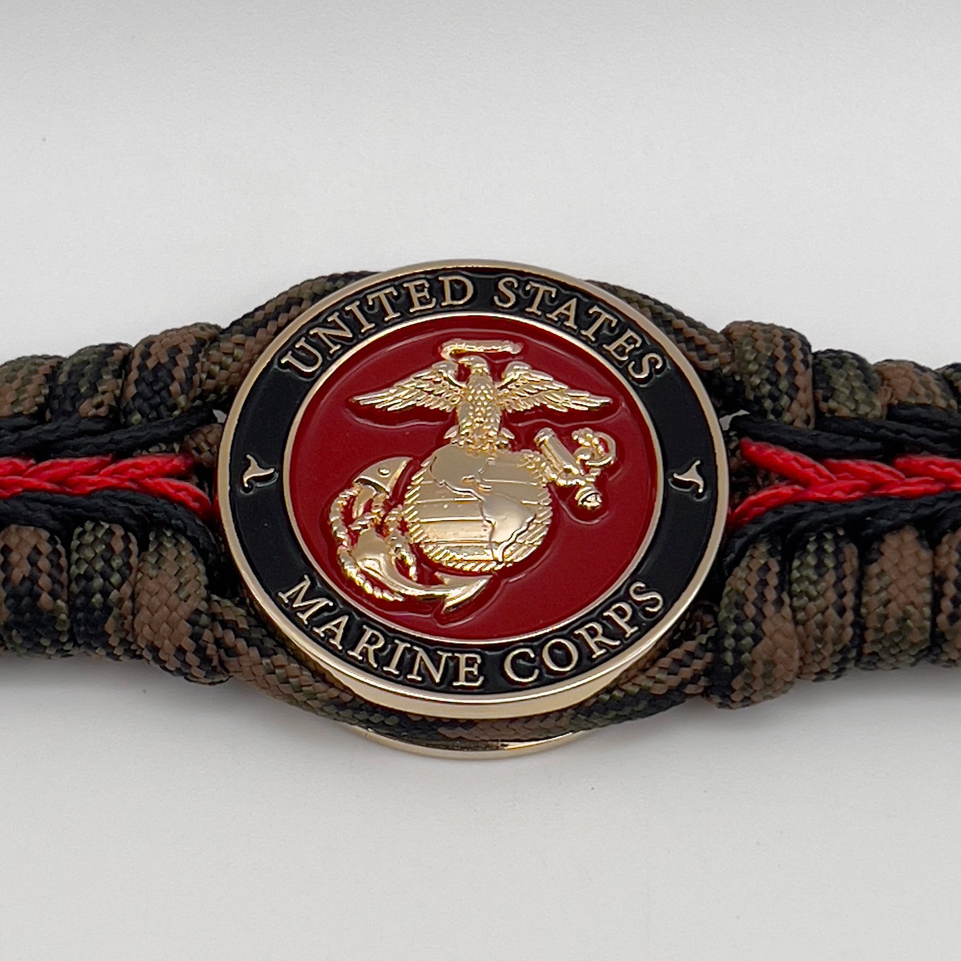Thick, semi-rigid and comfortable braided United States Marine Corps bracelet featuring a 24K gold plated USMC Eagle Globe and Anchor medallion, a gold Cobra style tactical buckle and woven with Woodland camo 550 paracord and black and Imperial red micro cord.