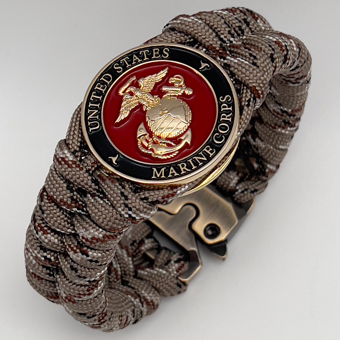 Thick, semi-rigid and comfortable braided United States Marine Corps bracelet featuring a 24K gold plated USMC Eagle Globe and Anchor medallion, a gold Cobra style tactical buckle and woven with Desert Camo 550 paracord.