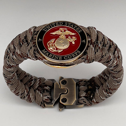 Thick, semi-rigid and comfortable braided United States Marine Corps bracelet featuring a 24K gold plated USMC Eagle Globe and Anchor medallion, a gold Cobra style tactical buckle and woven with Desert Camo 550 paracord.