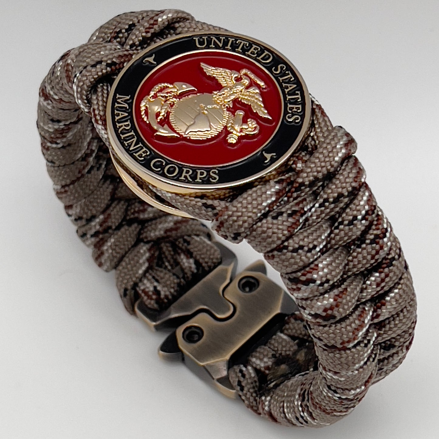 Thick, semi-rigid and comfortable braided United States Marine Corps bracelet featuring a 24K gold plated USMC Eagle Globe and Anchor medallion, a gold Cobra style tactical buckle and woven with Desert Camo 550 paracord.