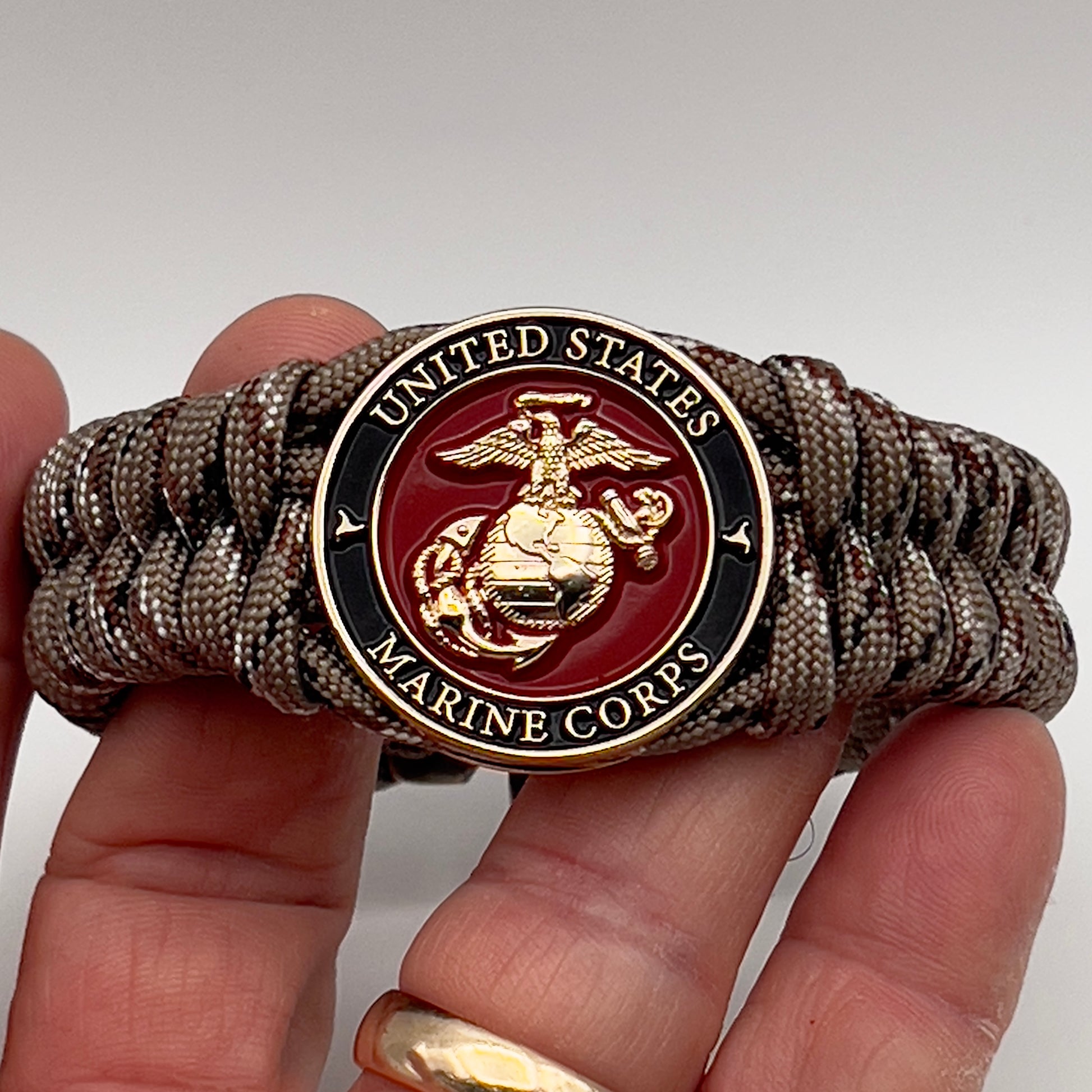 Thick, semi-rigid and comfortable braided United States Marine Corps bracelet featuring a 24K gold plated USMC Eagle Globe and Anchor medallion, a gold Cobra style tactical buckle and woven with Desert Camo 550 paracord.