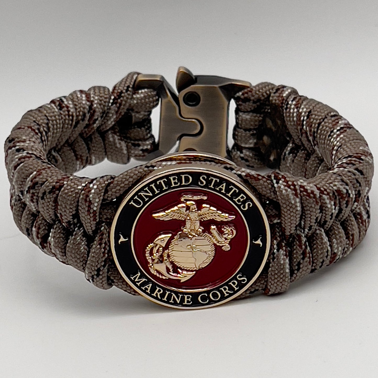 Thick, semi-rigid and comfortable braided United States Marine Corps bracelet featuring a 24K gold plated USMC Eagle Globe and Anchor medallion, a gold Cobra style tactical buckle and woven with Desert Camo 550 paracord.