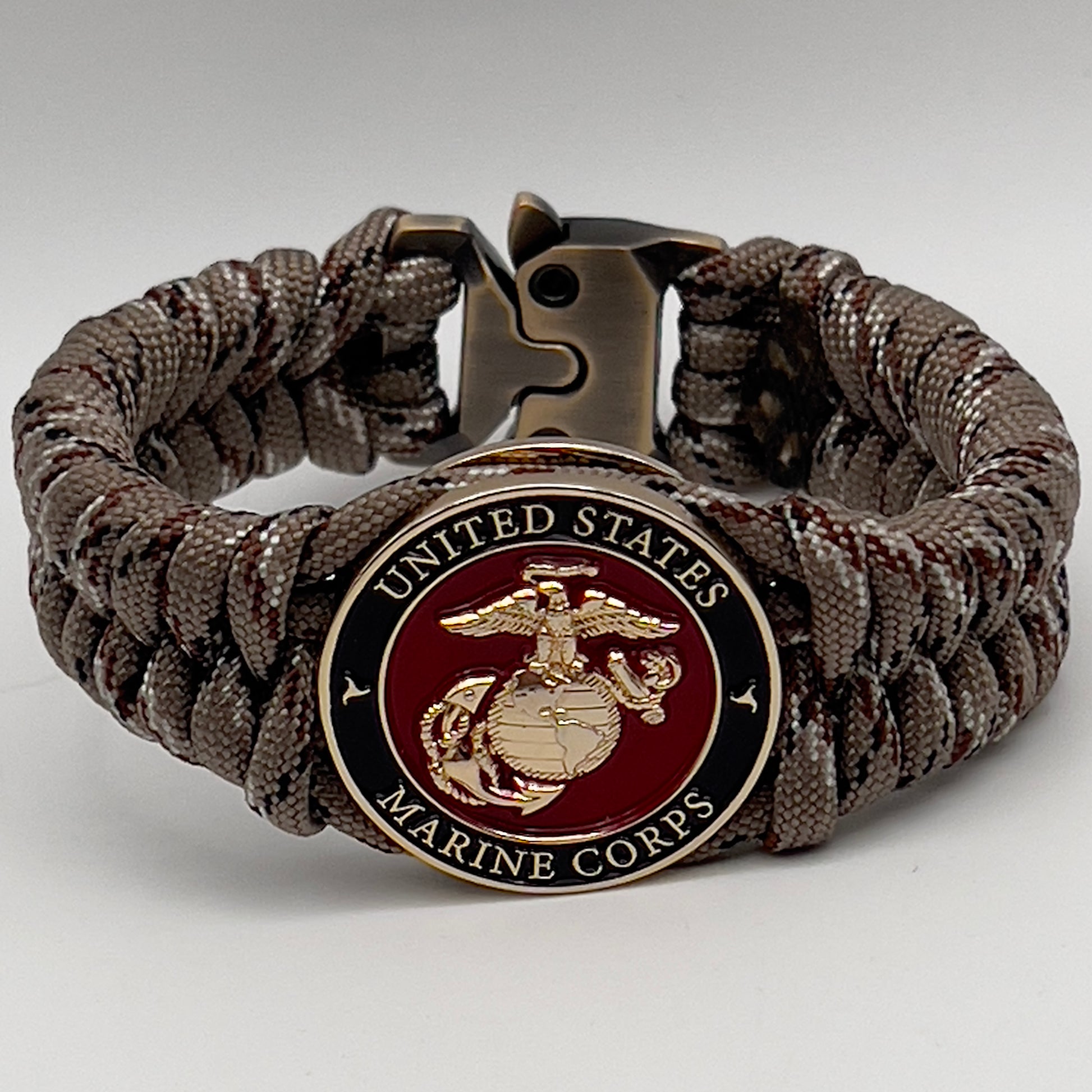 Thick, semi-rigid and comfortable braided United States Marine Corps bracelet featuring a 24K gold plated USMC Eagle Globe and Anchor medallion, a gold Cobra style tactical buckle and woven with Desert Camo 550 paracord.