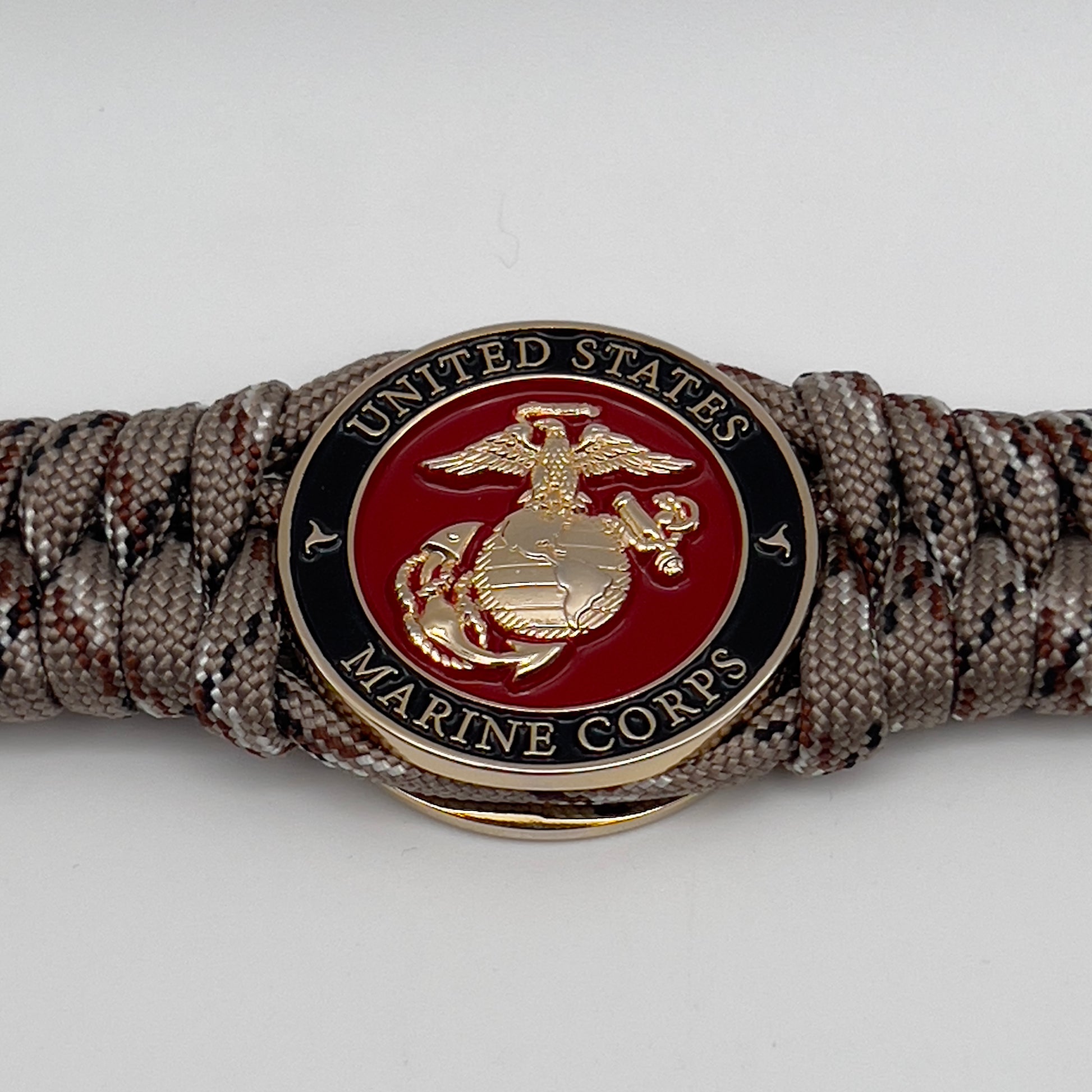 Thick, semi-rigid and comfortable braided United States Marine Corps bracelet featuring a 24K gold plated USMC Eagle Globe and Anchor medallion, a gold Cobra style tactical buckle and woven with Desert Camo 550 paracord.