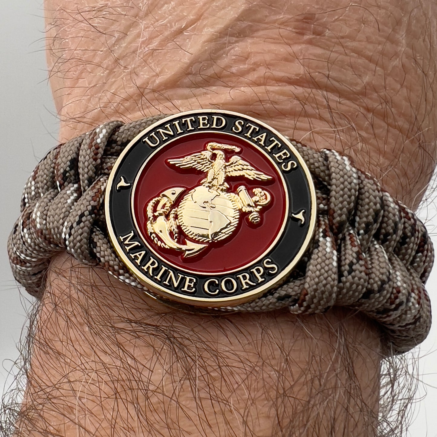 Thick, semi-rigid and comfortable braided United States Marine Corps bracelet featuring a 24K gold plated USMC Eagle Globe and Anchor medallion, a gold Cobra style tactical buckle and woven with Desert Camo 550 paracord.