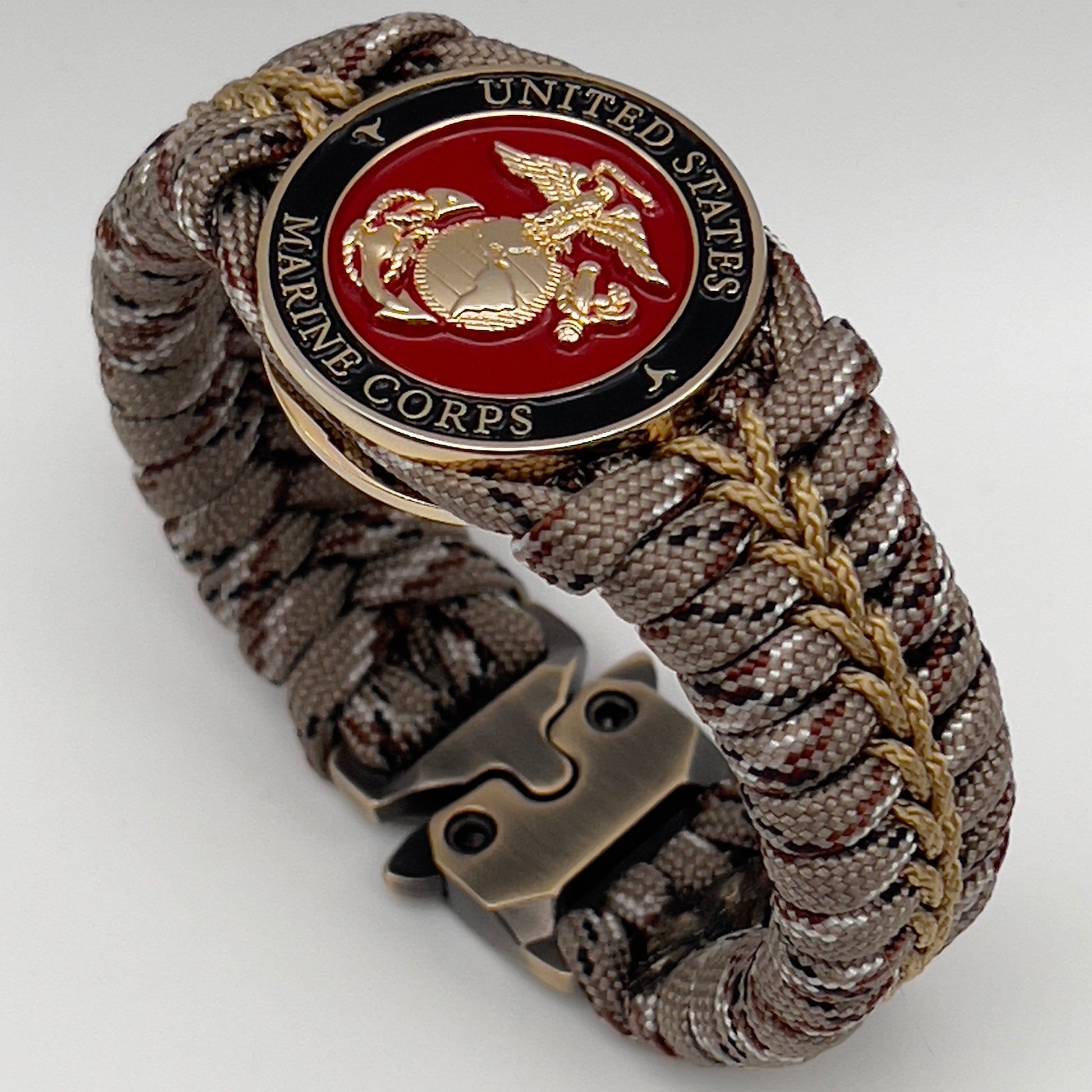 Thick, rigid and comfortable braided United States Marine Corps bracelet featuring a 24K gold plated USMC Eagle Globe and Anchor medallion, a gold Cobra style tactical buckle and woven with Desert Camo 550 paracord.
