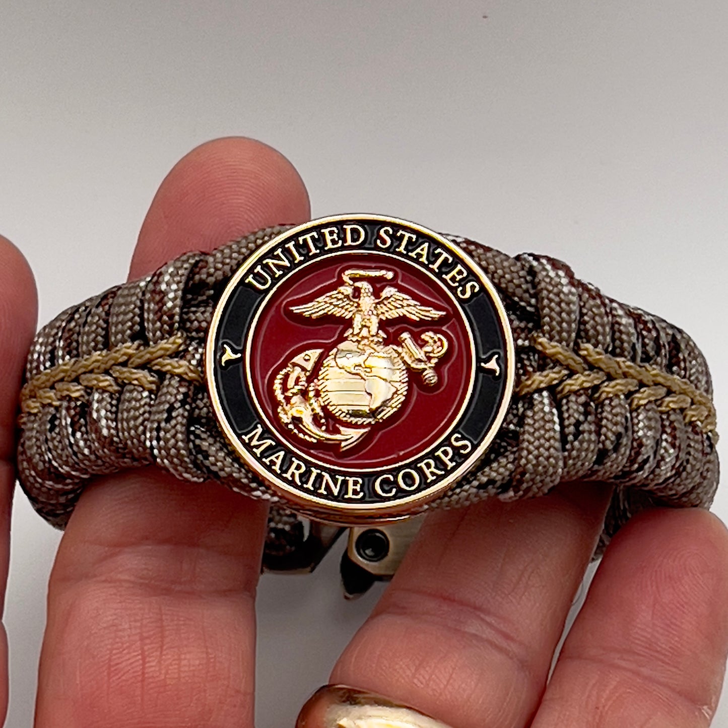 Thick, rigid and comfortable braided United States Marine Corps bracelet featuring a 24K gold plated USMC Eagle Globe and Anchor medallion, a gold Cobra style tactical buckle and woven with Desert Camo 550 paracord.