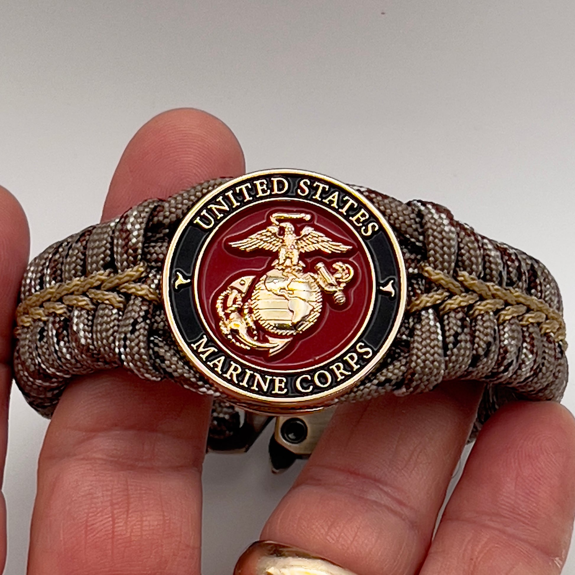 Thick, rigid and comfortable braided United States Marine Corps bracelet featuring a 24K gold plated USMC Eagle Globe and Anchor medallion, a gold Cobra style tactical buckle and woven with Desert Camo 550 paracord.