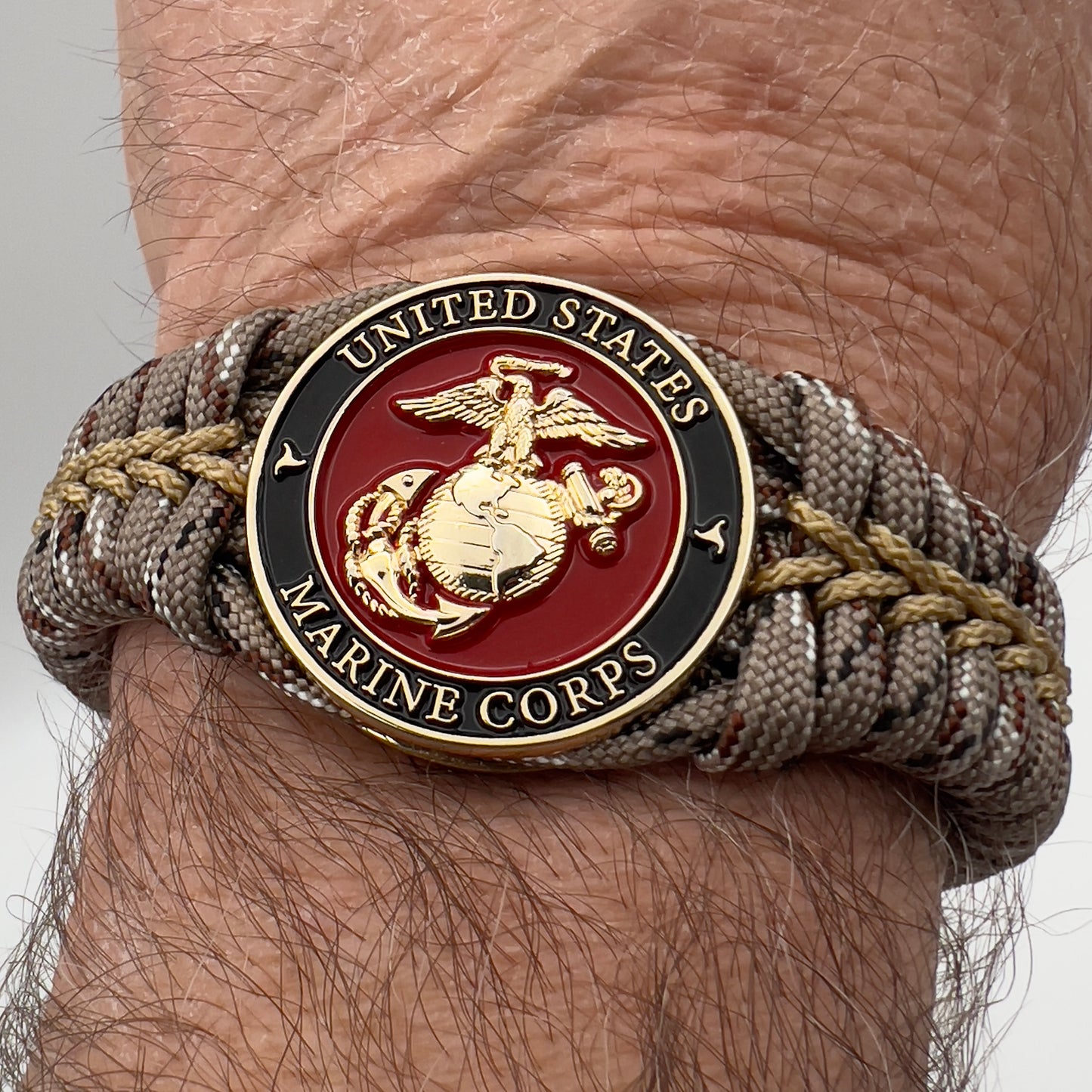 Thick, rigid and comfortable braided United States Marine Corps bracelet featuring a 24K gold plated USMC Eagle Globe and Anchor medallion, a gold Cobra style tactical buckle and woven with Desert Camo 550 paracord.