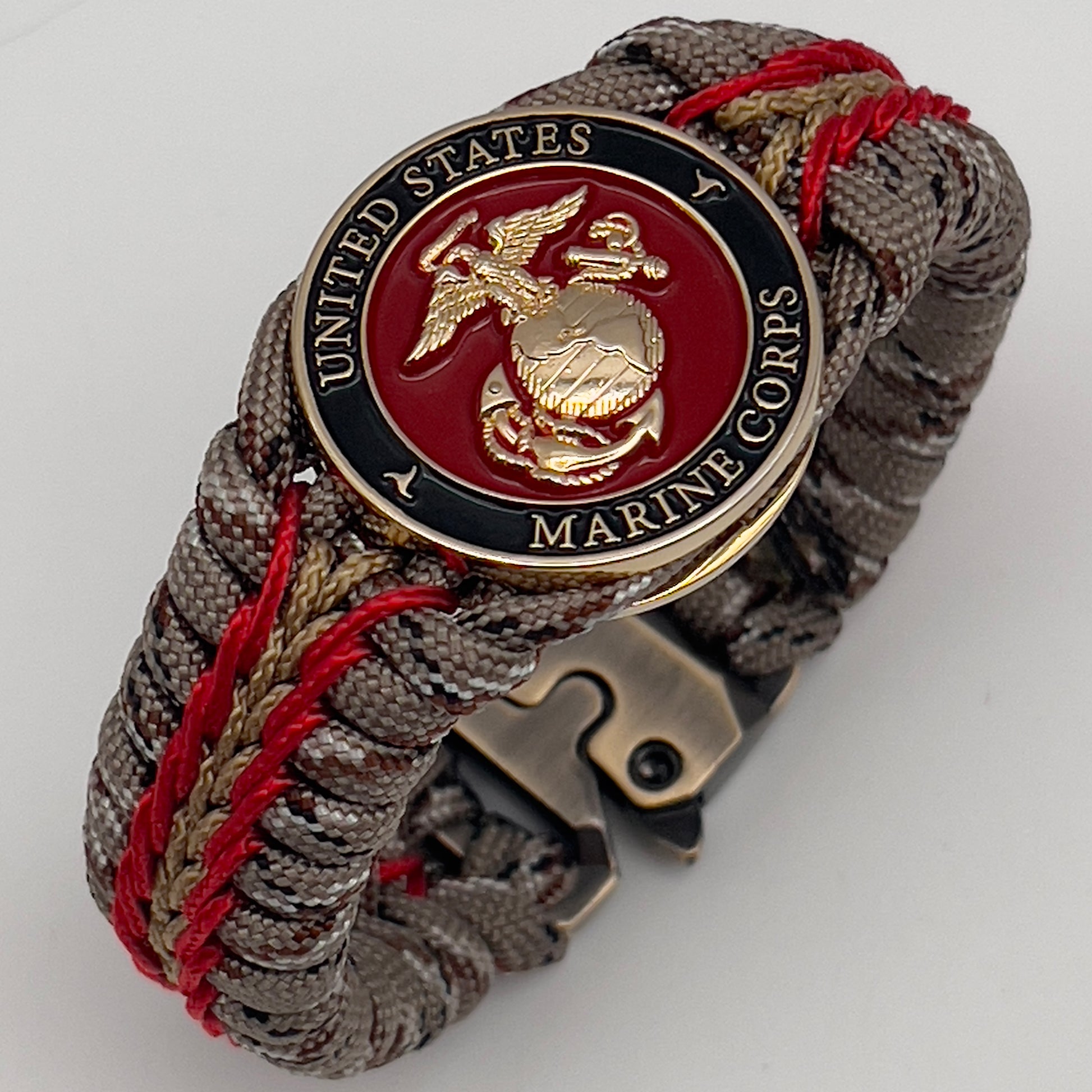 Thick, rigid and comfortable braided United States Marine Corps bracelet featuring a 24K gold plated USMC Eagle Globe and Anchor medallion, a gold Cobra style tactical buckle and woven with Desert Camo 550 paracord and Imperial Red and Gold micro cord.
