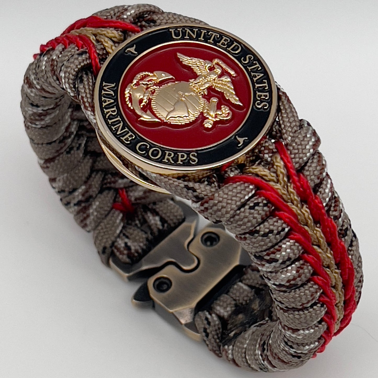 Thick, rigid and comfortable braided United States Marine Corps bracelet featuring a 24K gold plated USMC Eagle Globe and Anchor medallion, a gold Cobra style tactical buckle and woven with Desert Camo 550 paracord and Imperial Red and Gold micro cord.