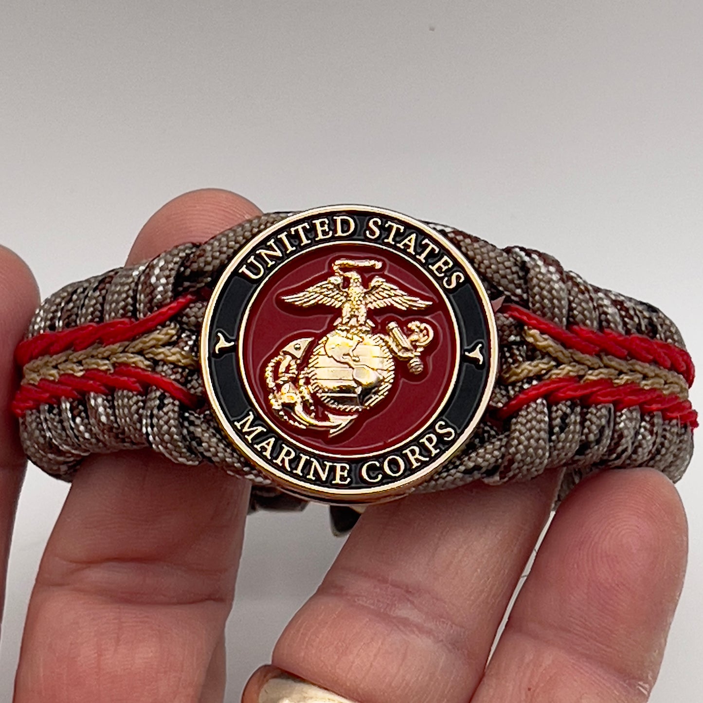 Thick, rigid and comfortable braided United States Marine Corps bracelet featuring a 24K gold plated USMC Eagle Globe and Anchor medallion, a gold Cobra style tactical buckle and woven with Desert Camo 550 paracord and Imperial Red and Gold micro cord.