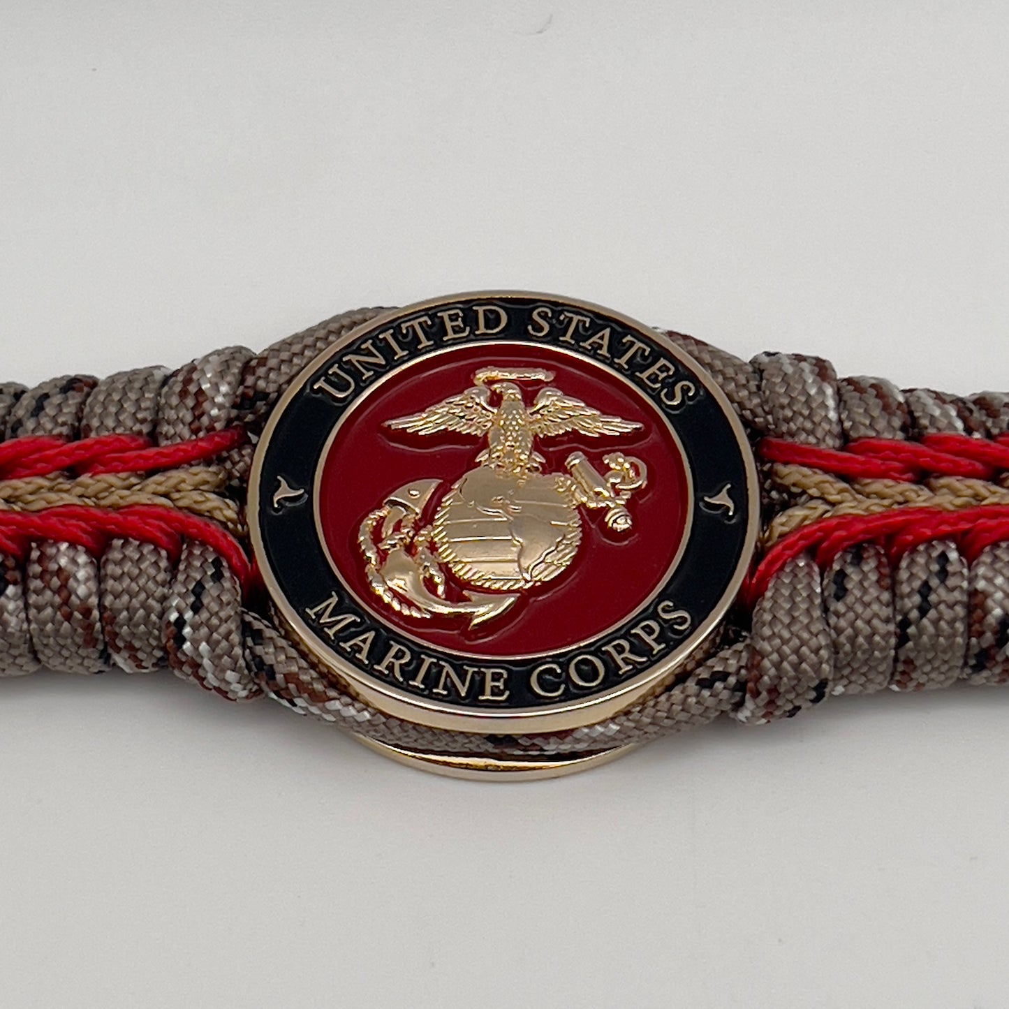 Thick, rigid and comfortable braided United States Marine Corps bracelet featuring a 24K gold plated USMC Eagle Globe and Anchor medallion, a gold Cobra style tactical buckle and woven with Desert Camo 550 paracord and Imperial Red and Gold micro cord.