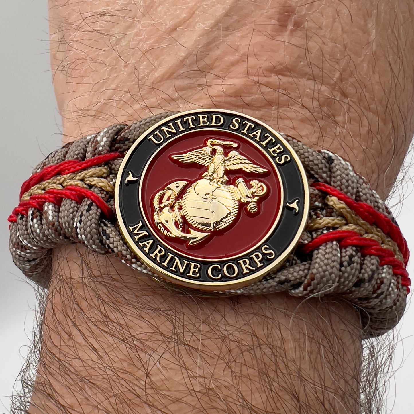 Thick, rigid and comfortable braided United States Marine Corps bracelet featuring a 24K gold plated USMC Eagle Globe and Anchor medallion, a gold Cobra style tactical buckle and woven with Desert Camo 550 paracord and Imperial Red and Gold micro cord.