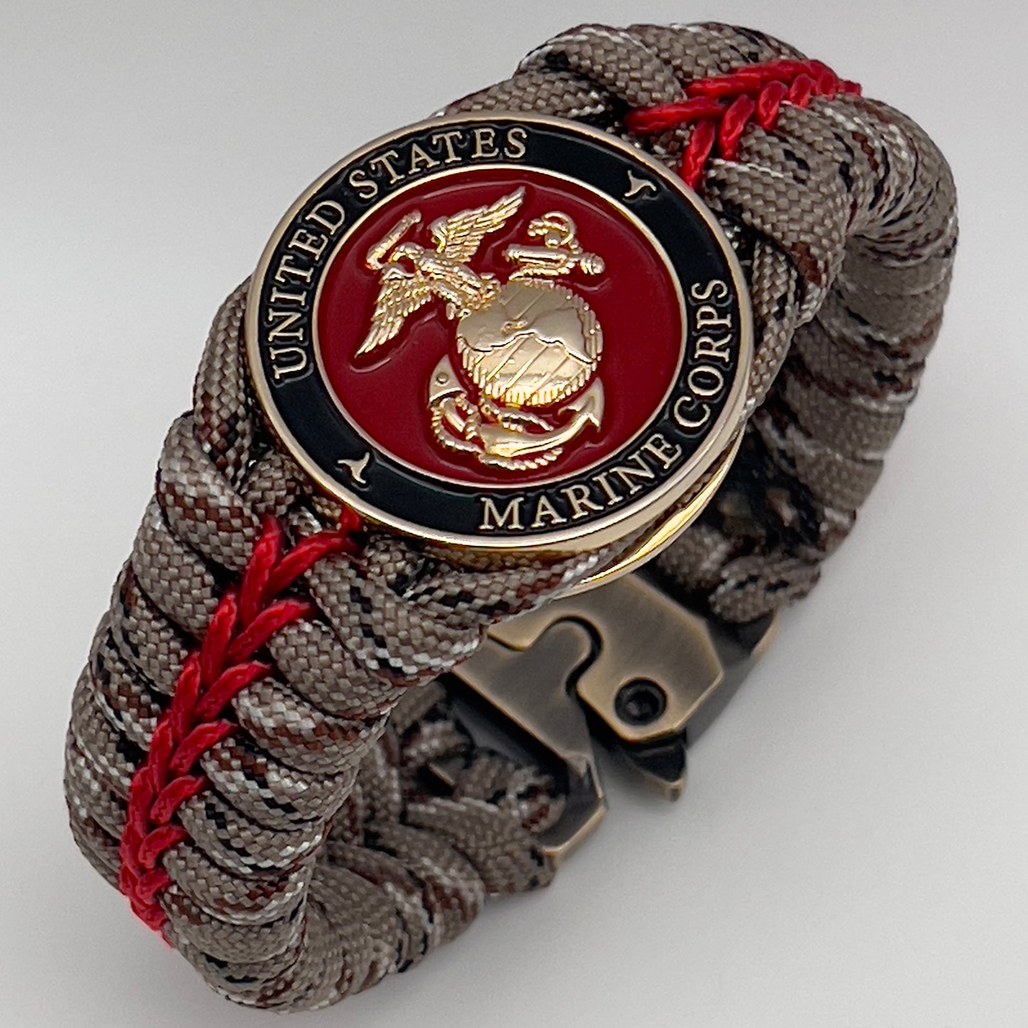 Thick, rigid and comfortable braided United States Marine Corps bracelet featuring a 24K gold plated USMC Eagle Globe and Anchor medallion, a gold Cobra style tactical buckle and woven with Desert Camo 550 paracord and Imperial Red micro cord.