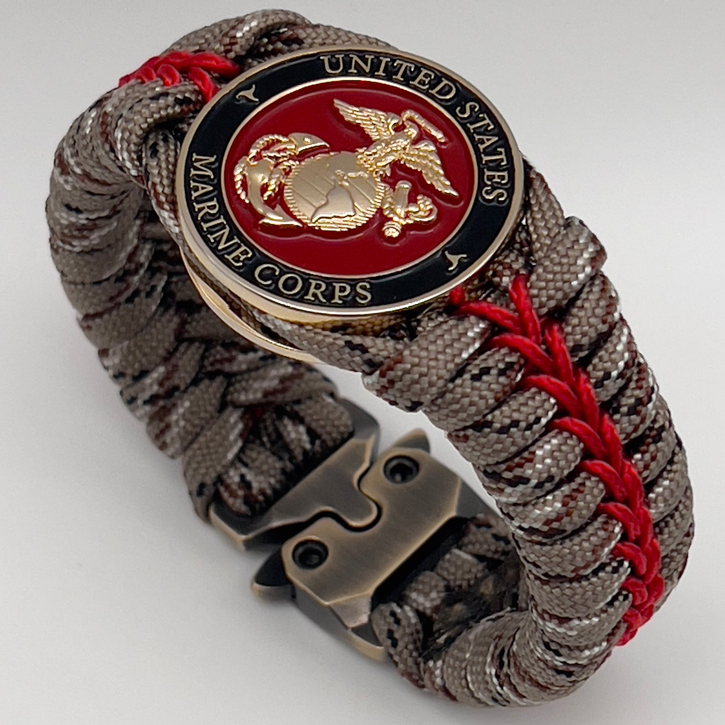 Thick, rigid and comfortable braided United States Marine Corps bracelet featuring a 24K gold plated USMC Eagle Globe and Anchor medallion, a gold Cobra style tactical buckle and woven with Desert Camo 550 paracord and Imperial Red micro cord.