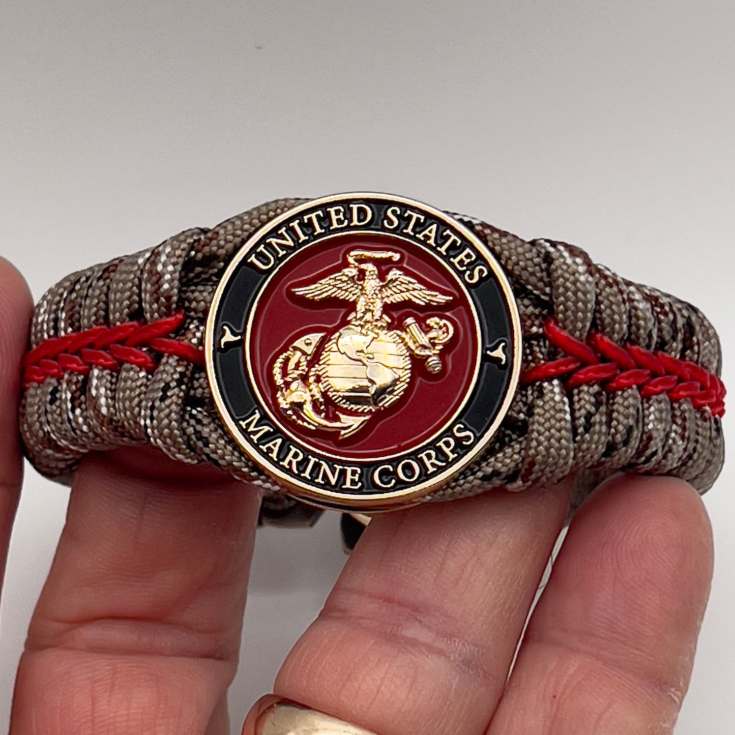 Thick, rigid and comfortable braided United States Marine Corps bracelet featuring a 24K gold plated USMC Eagle Globe and Anchor medallion, a gold Cobra style tactical buckle and woven with Desert Camo 550 paracord and Imperial Red micro cord.