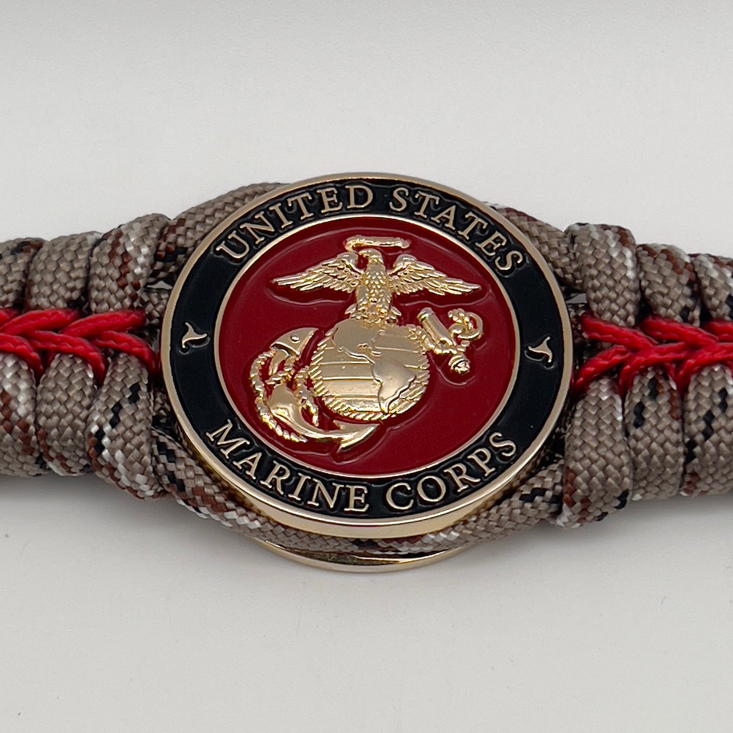 Thick, rigid and comfortable braided United States Marine Corps bracelet featuring a 24K gold plated USMC Eagle Globe and Anchor medallion, a gold Cobra style tactical buckle and woven with Desert Camo 550 paracord and Imperial Red micro cord.