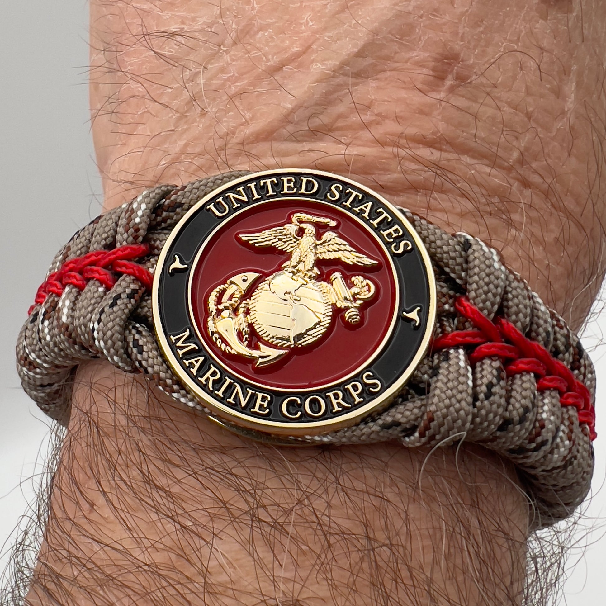 Thick, rigid and comfortable braided United States Marine Corps bracelet featuring a 24K gold plated USMC Eagle Globe and Anchor medallion, a gold Cobra style tactical buckle and woven with Desert Camo 550 paracord and Imperial Red micro cord.