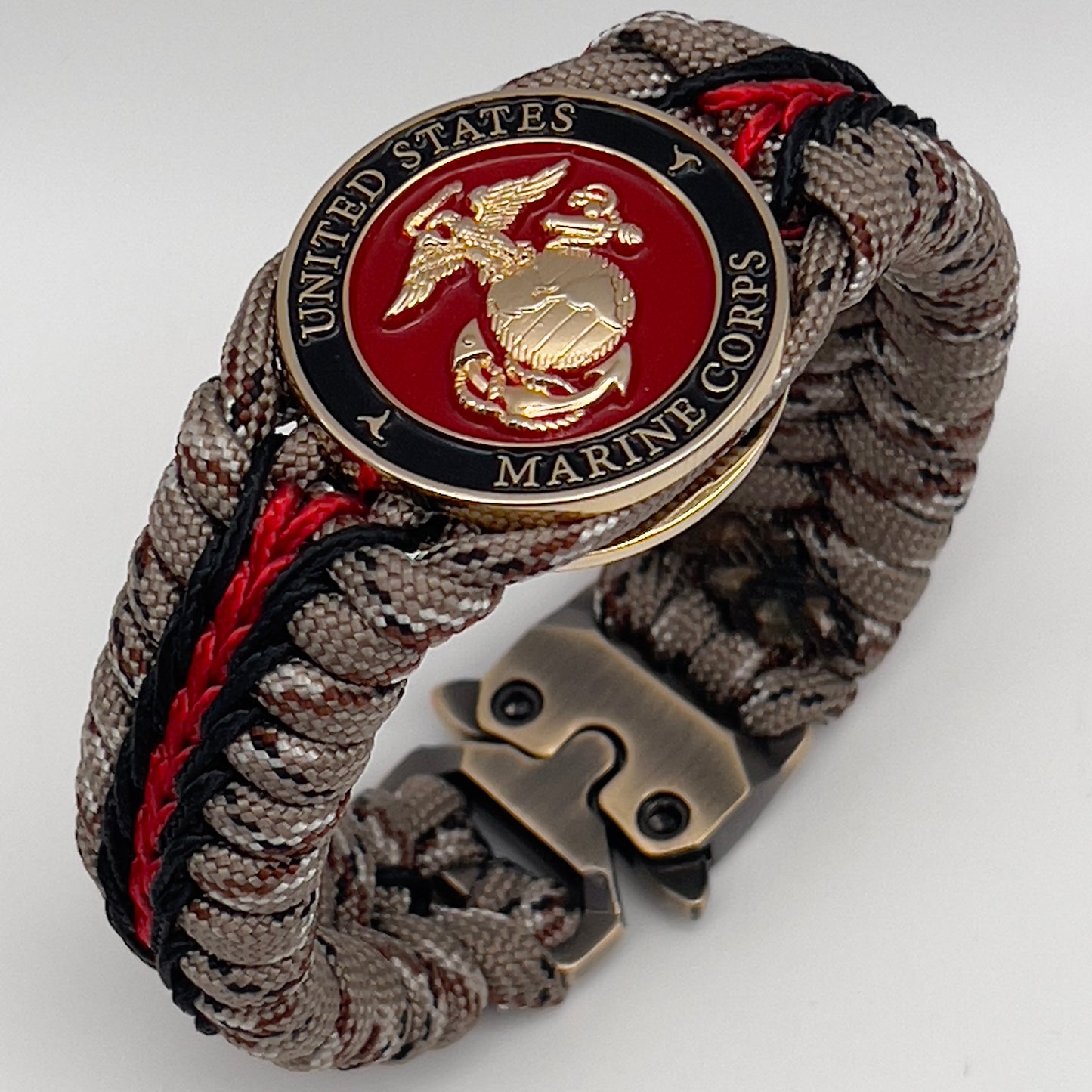 Thick, rigid and comfortable braided United States Marine Corps bracelet featuring a 24K gold plated USMC Eagle Globe and Anchor medallion, a gold Cobra style tactical buckle and woven with Desert Camo 550 paracord and black and Imperial Red micro cord.